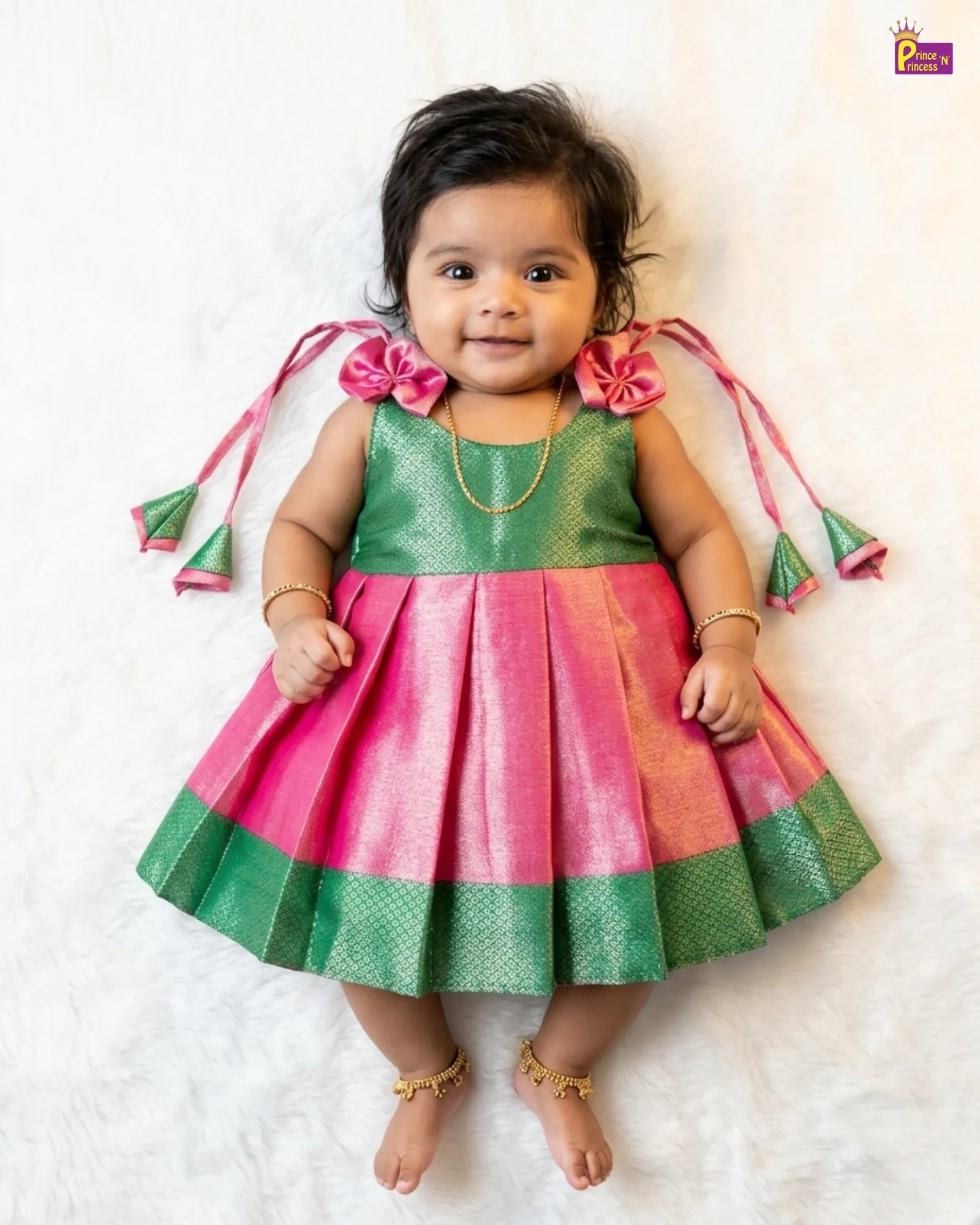 Baby wearing a green and pink traditional outfit with decorative elements on a white background