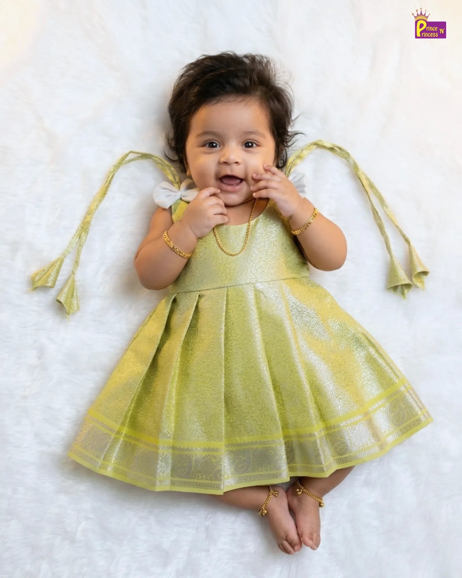 Baby in a yellow dress lying on a white surface