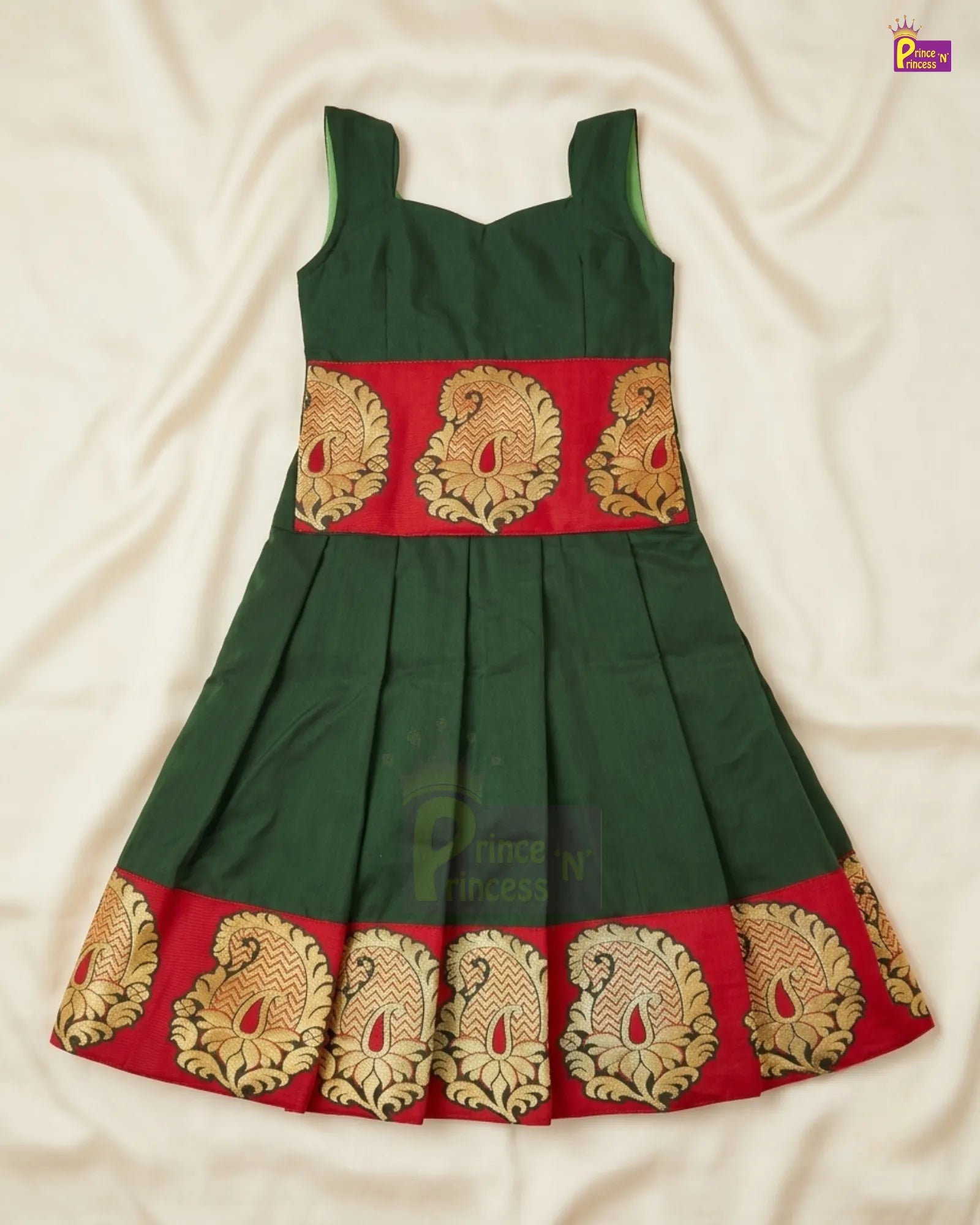 A dark green sleeveless dress with a red band featuring gold and beige peacock motifs, laid flat on a cream-colored fabric background.