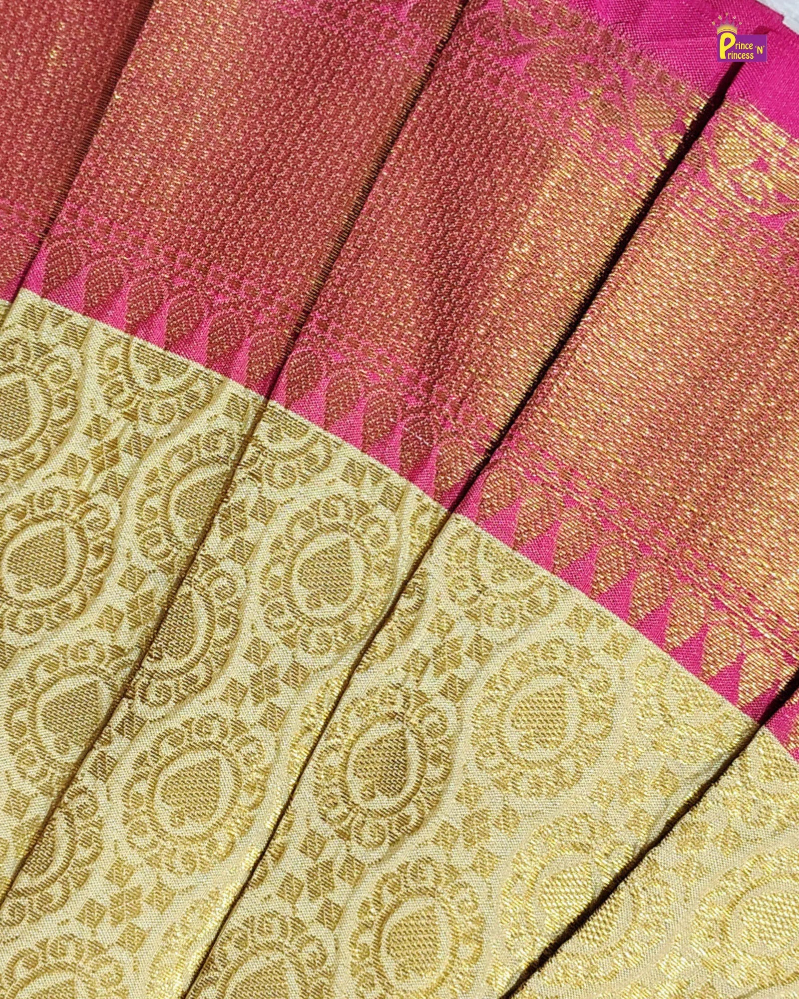 A close-up of a woven textile, likely a sari, featuring a rich magenta-pink and gold body with a wide beige-gold brocade border and a bright pink edge.