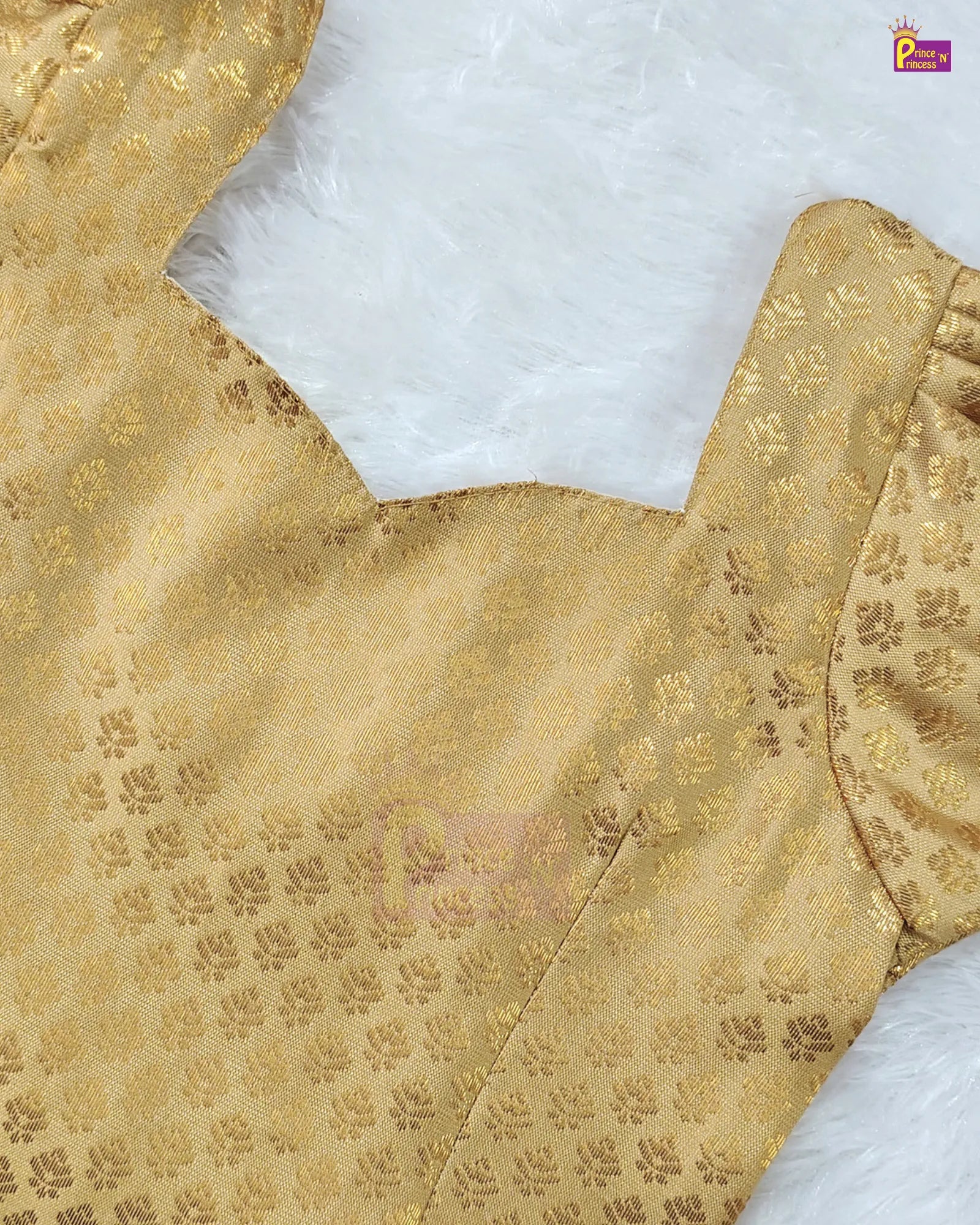 Close-up of a gold brocade blouse fabric with a repeating floral pattern, laid flat on a white faux fur surface.