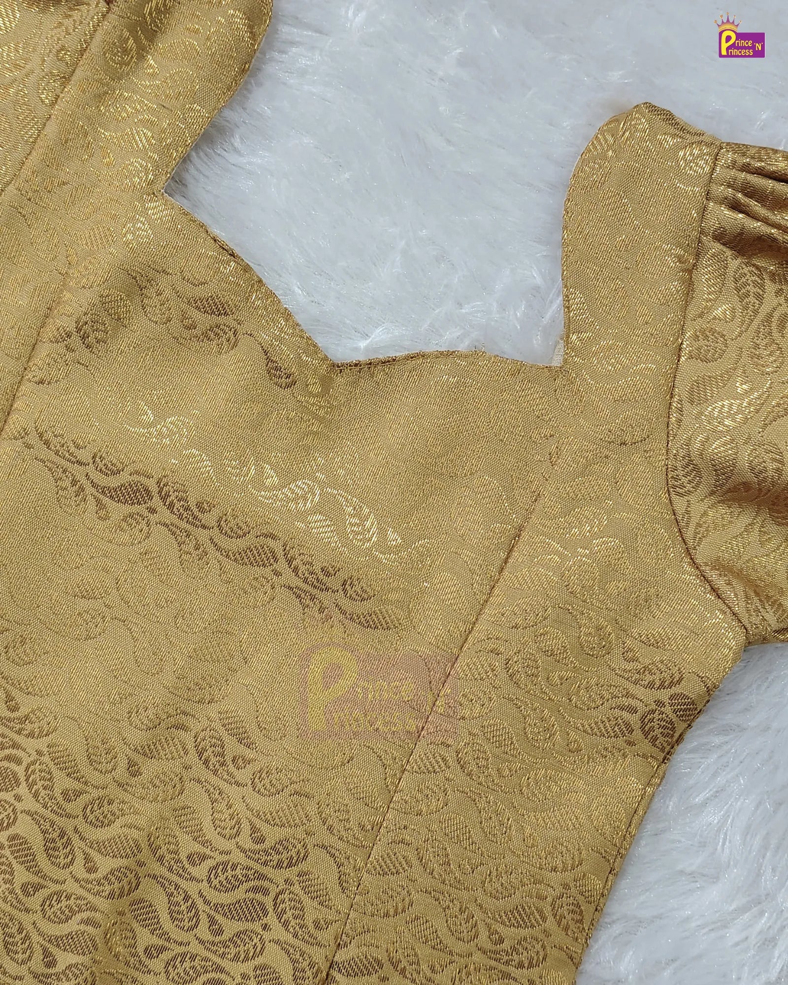 Close-up of a gold jacquard blouse fabric with a floral brocade pattern, laid flat on a white faux fur surface.