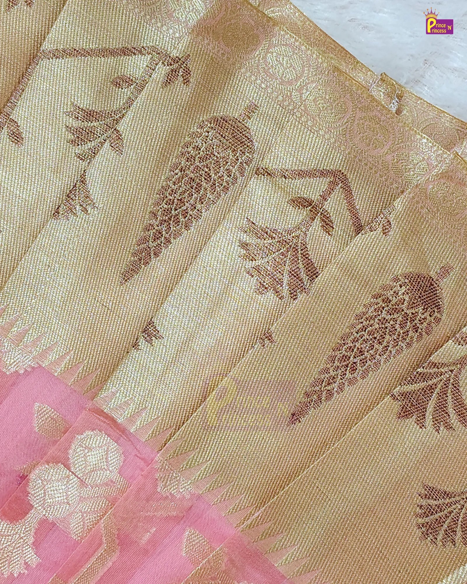 A close-up of a beige and gold saree fabric with woven botanical motifs, featuring a pink border with gold floral details.
