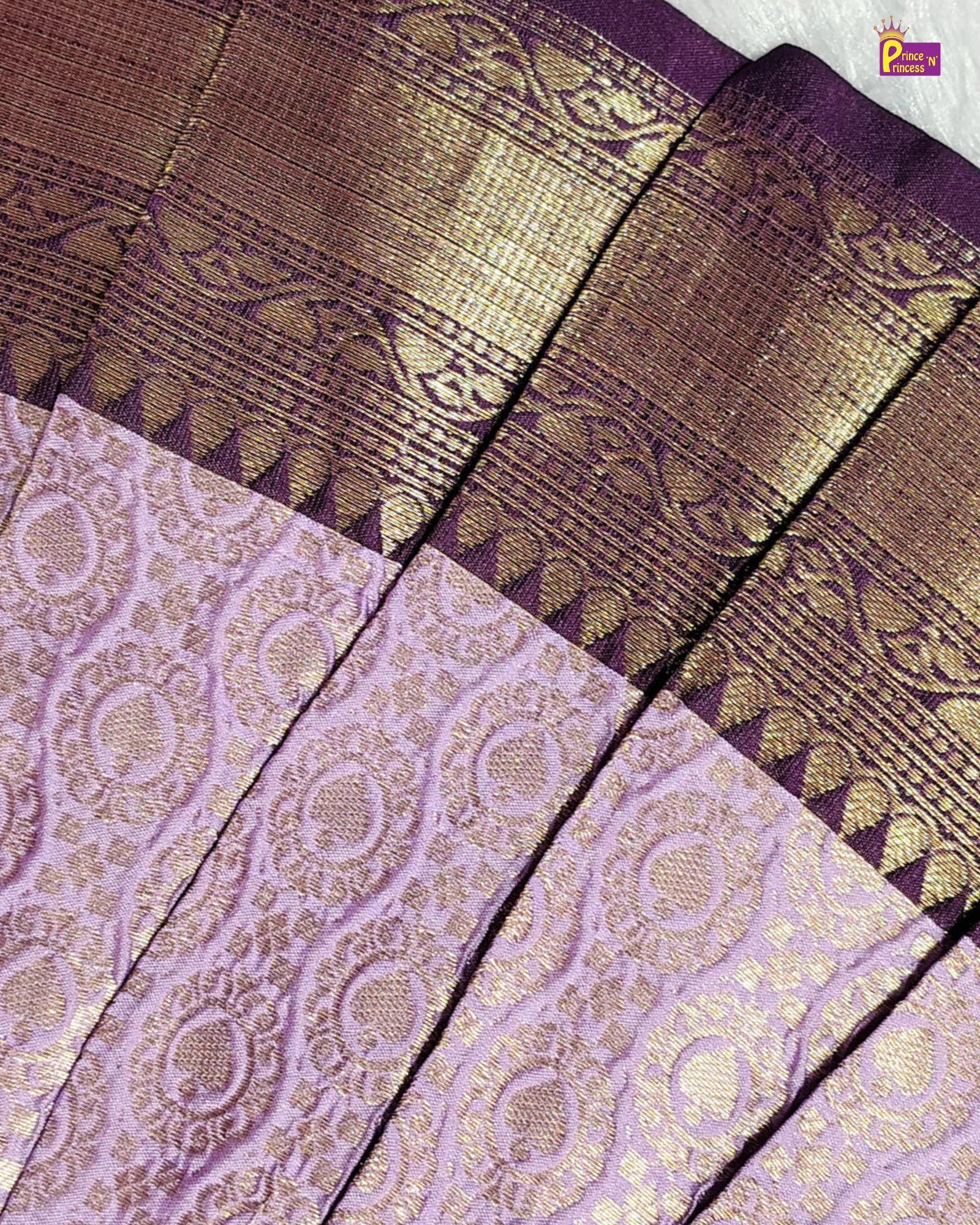 Close-up of a traditional Indian silk saree fabric with a lavender purple body, intricate gold zari woven patterns, and a wide metallic gold and purple border.