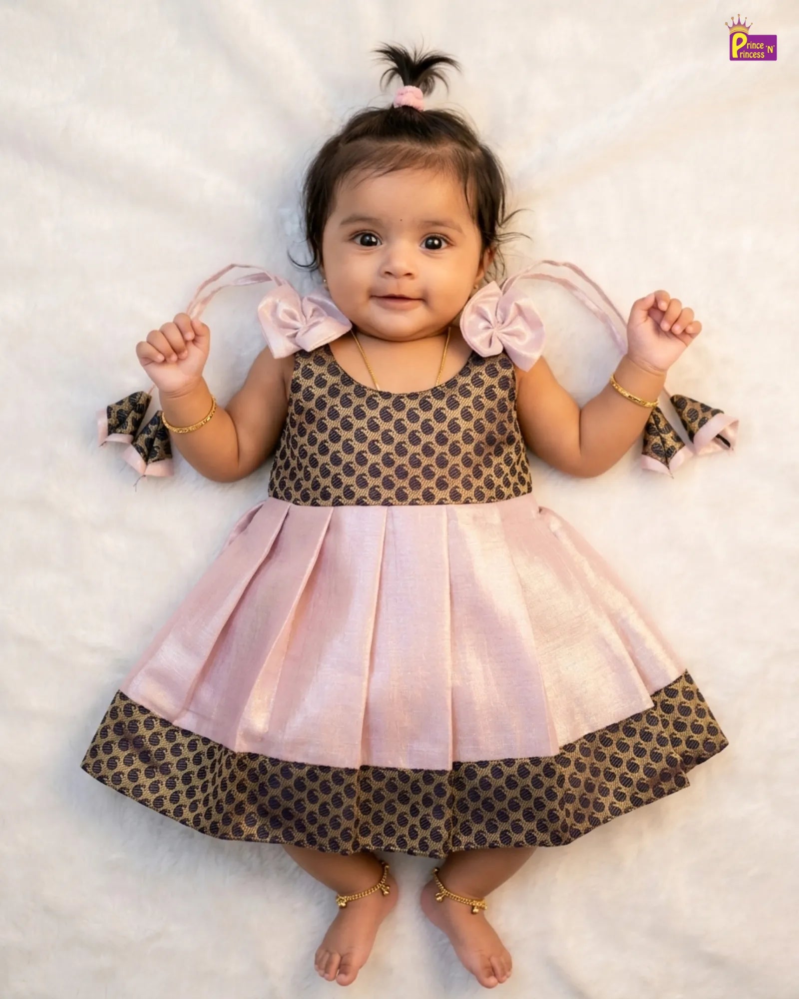 Baby wearing a pink and brown dress with ruffled sleeves on a white background