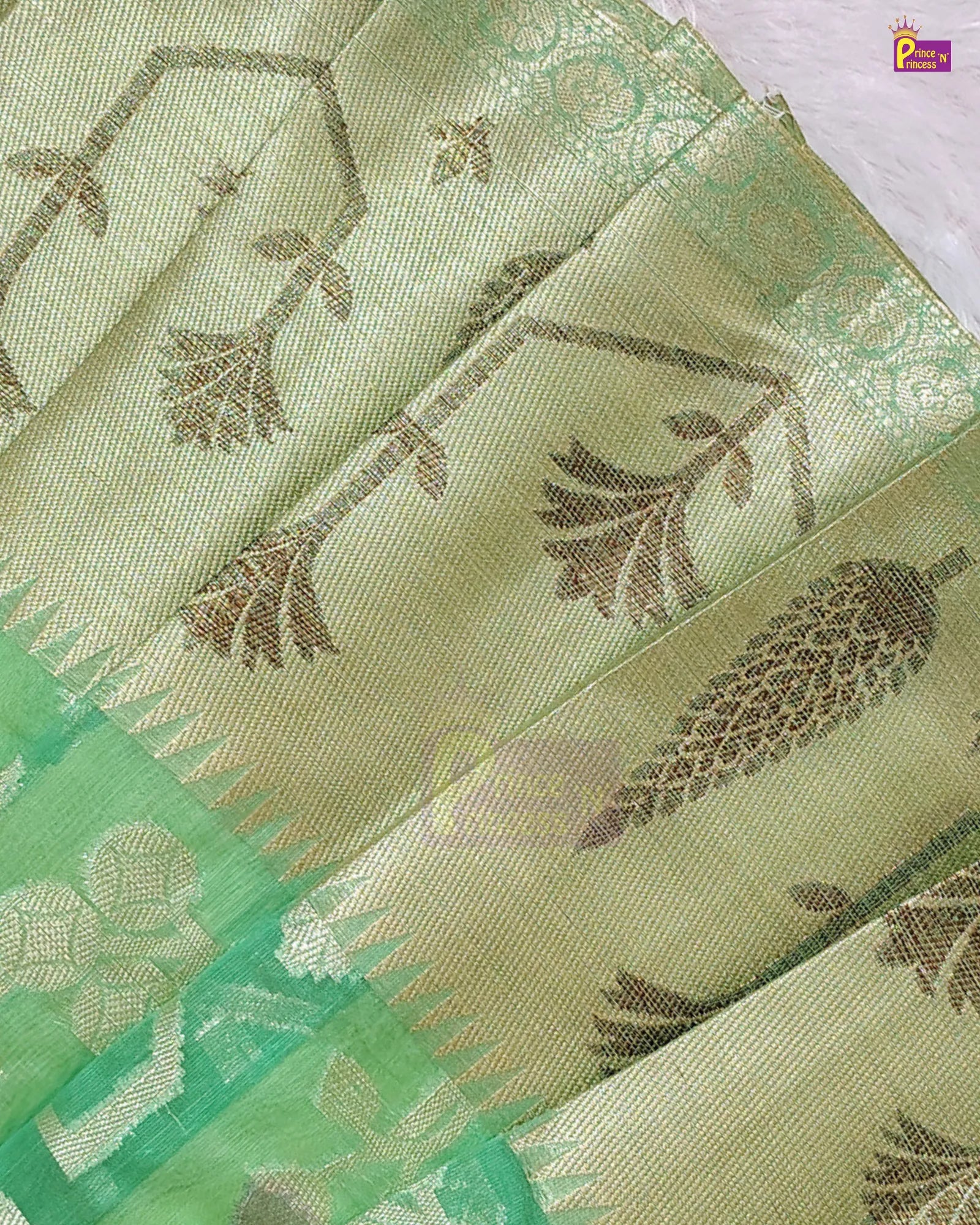 A close-up of a light green silk saree with metallic gold floral and vine motifs woven across the fabric, featuring a contrasting green border.