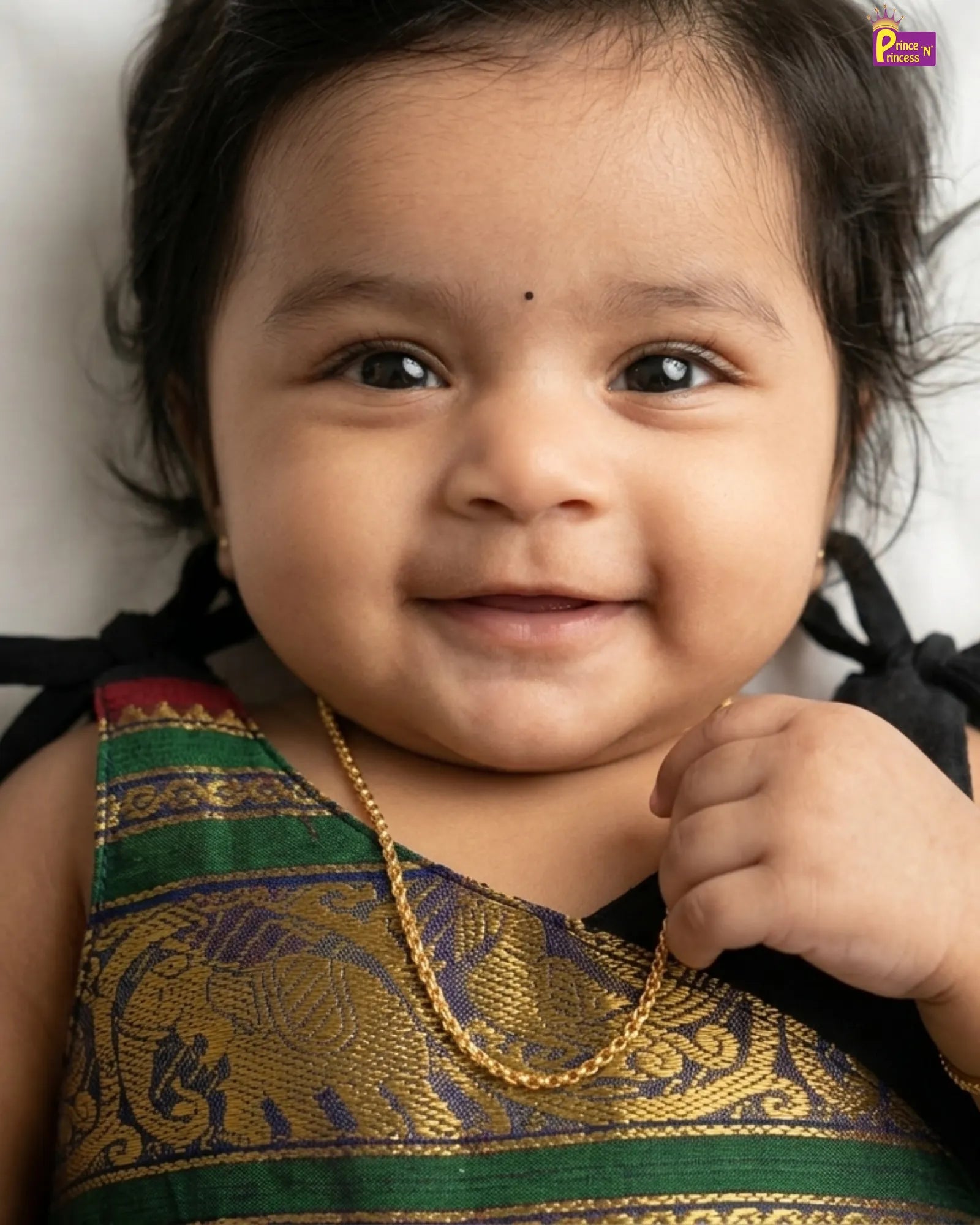 Baby wearing a traditional outfit with a gold necklace against a neutral background