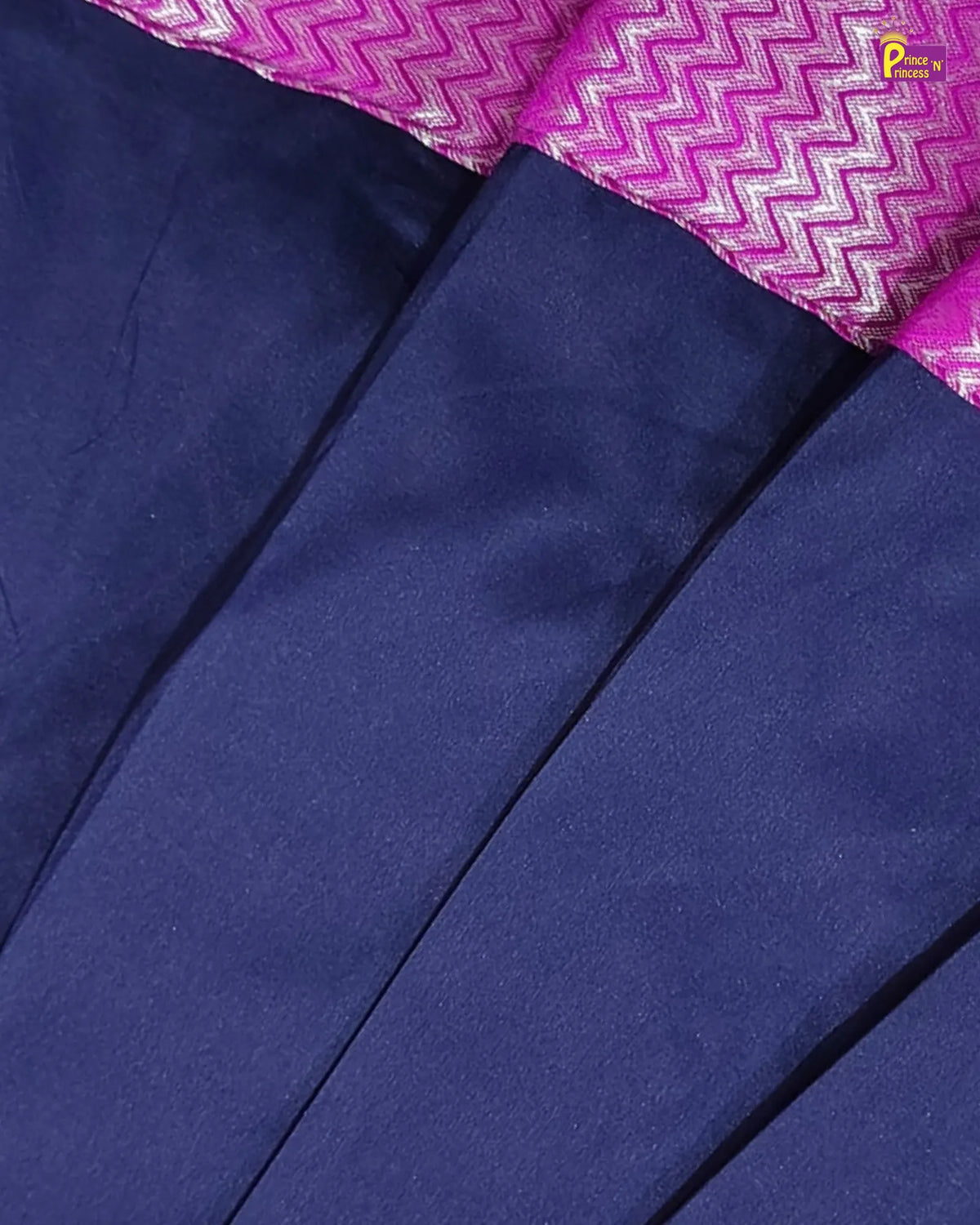 Close-up of a navy blue fabric garment with a folded hem showing a bright pink and white zigzag patterned border.
