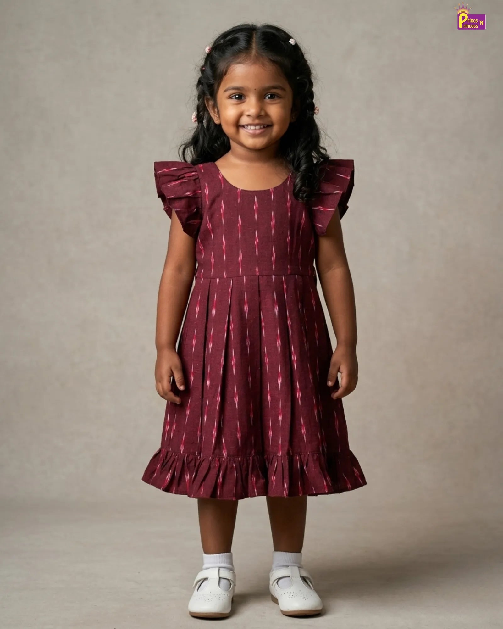 Young girl wearing a maroon dress with ruffled sleeves against a plain background