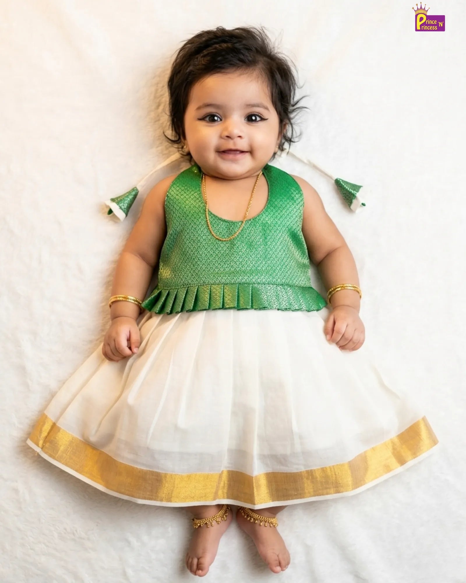 Baby wearing a green and white traditional outfit with gold accents on a light background