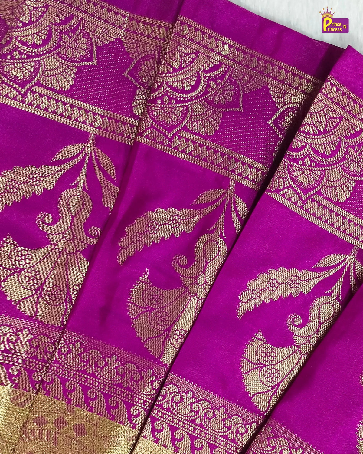 A close-up of a rich magenta purple silk saree with intricate gold zari brocade work, featuring traditional Indian motifs and borders.