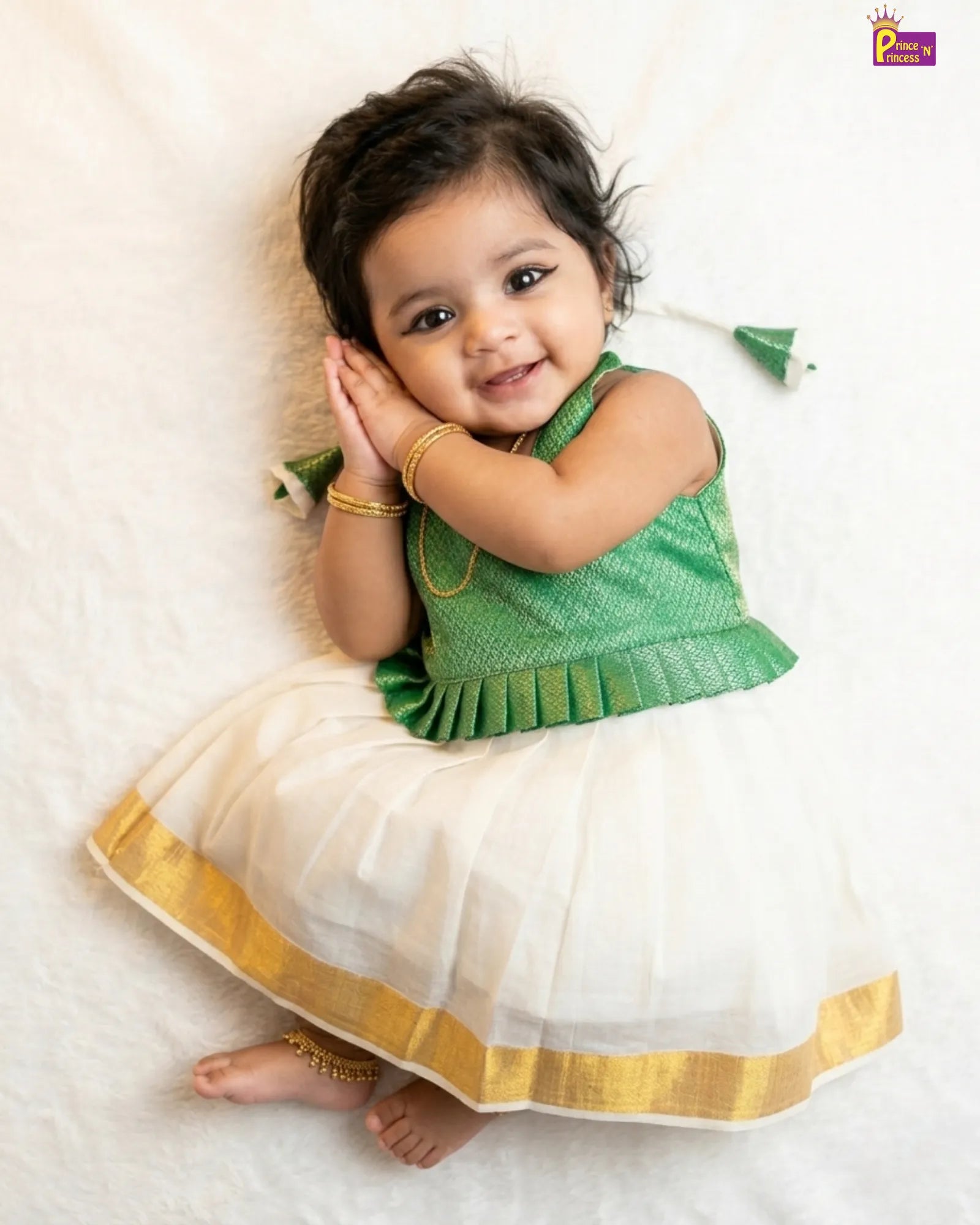 Baby wearing a green and white traditional outfit with gold trim on a light background