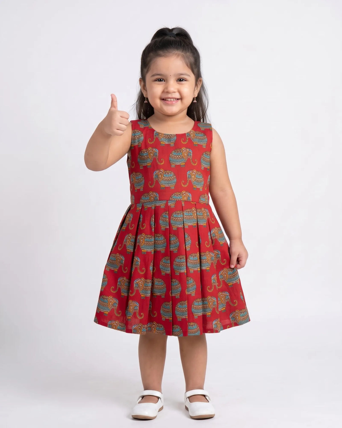 A young girl with dark hair wearing a magenta traditional Indian dress with gold and blue zari borders, standing against a plain light beige background.
