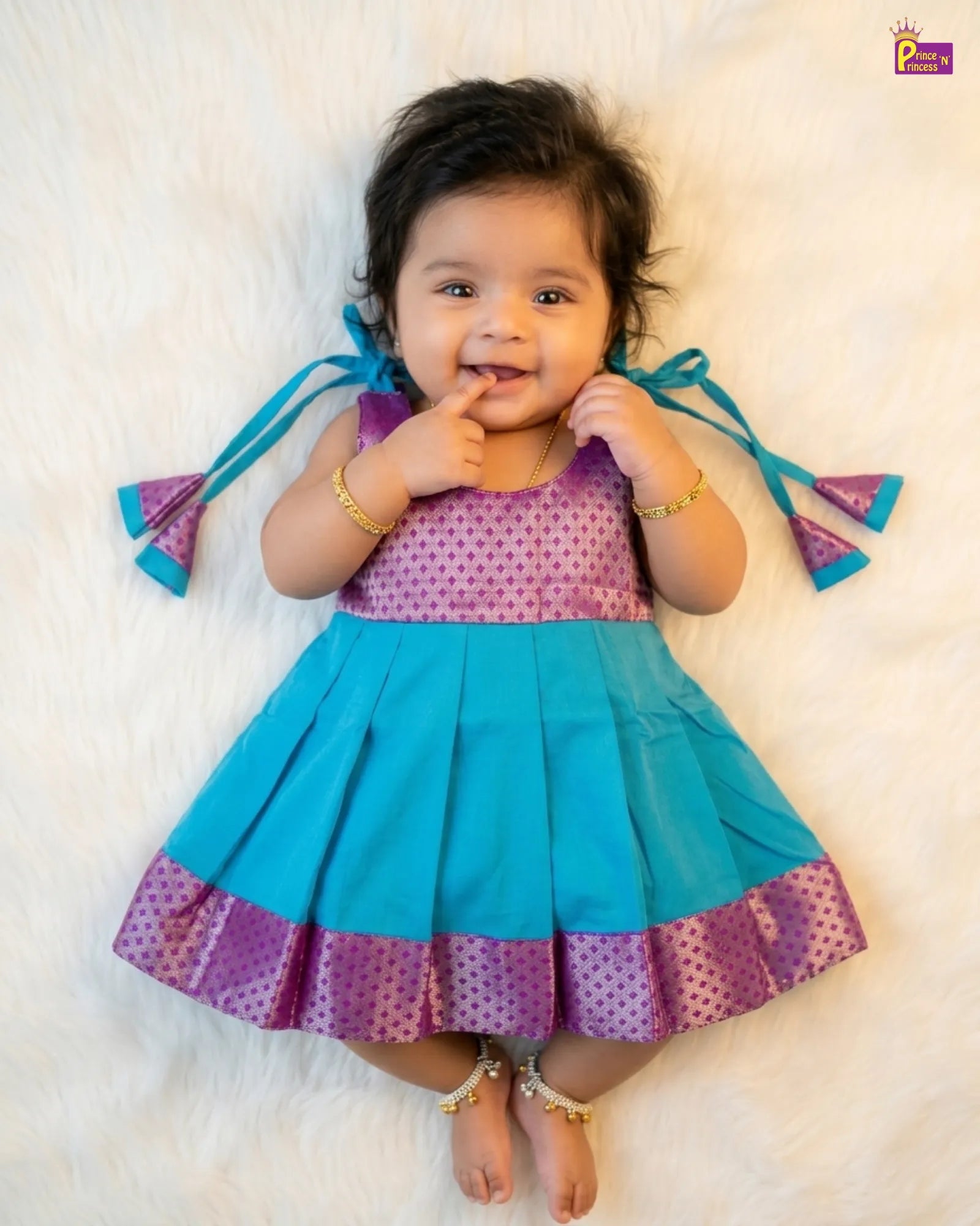 Baby wearing a colorful dress with blue and purple accents on a white background