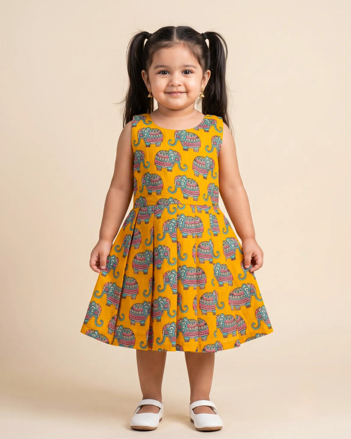 A young girl modeling a traditional Indian salwar kameez dress in maroon with gold and green borders, set against a plain beige studio background.