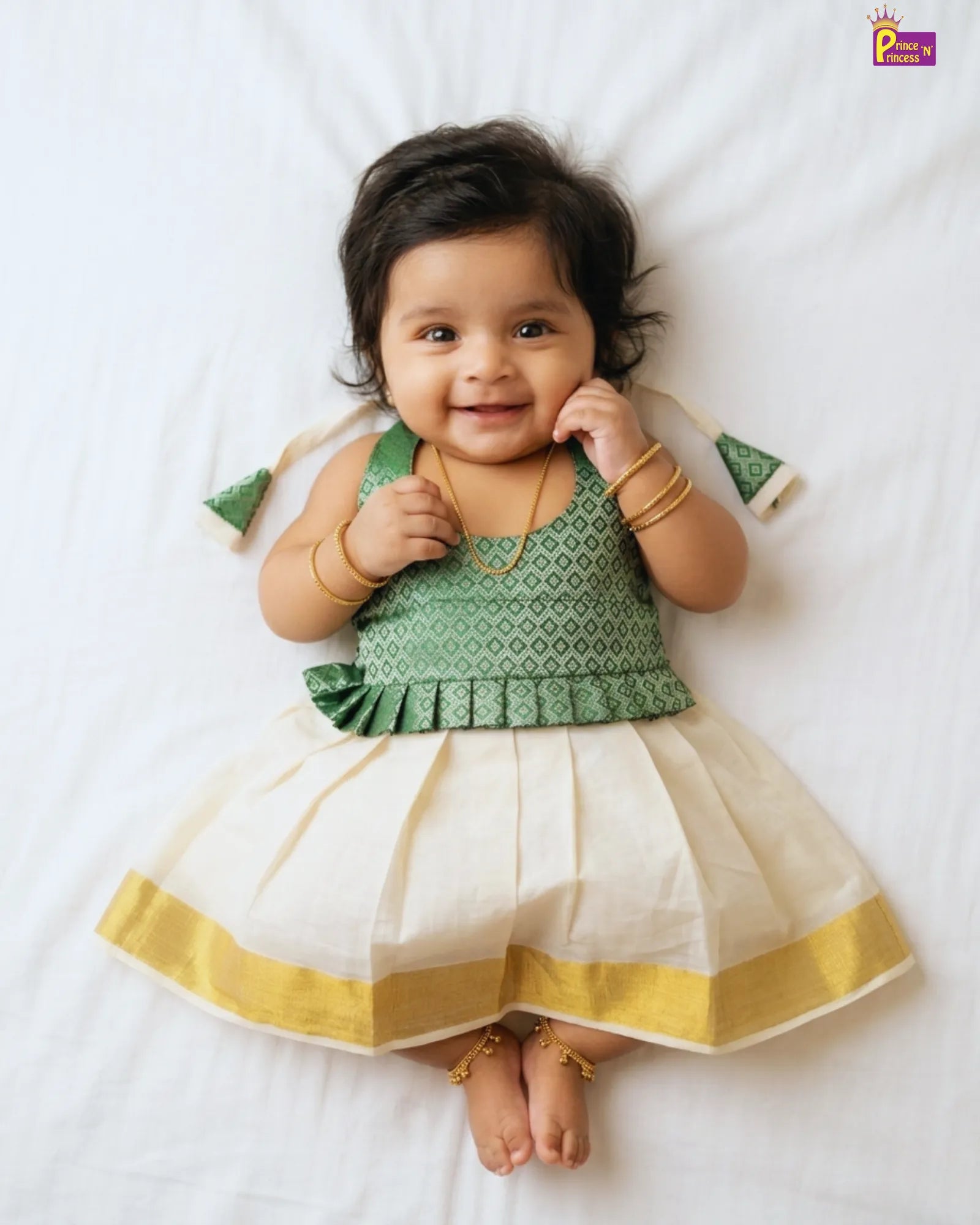 Baby wearing a green and white traditional outfit with gold accents on a white background