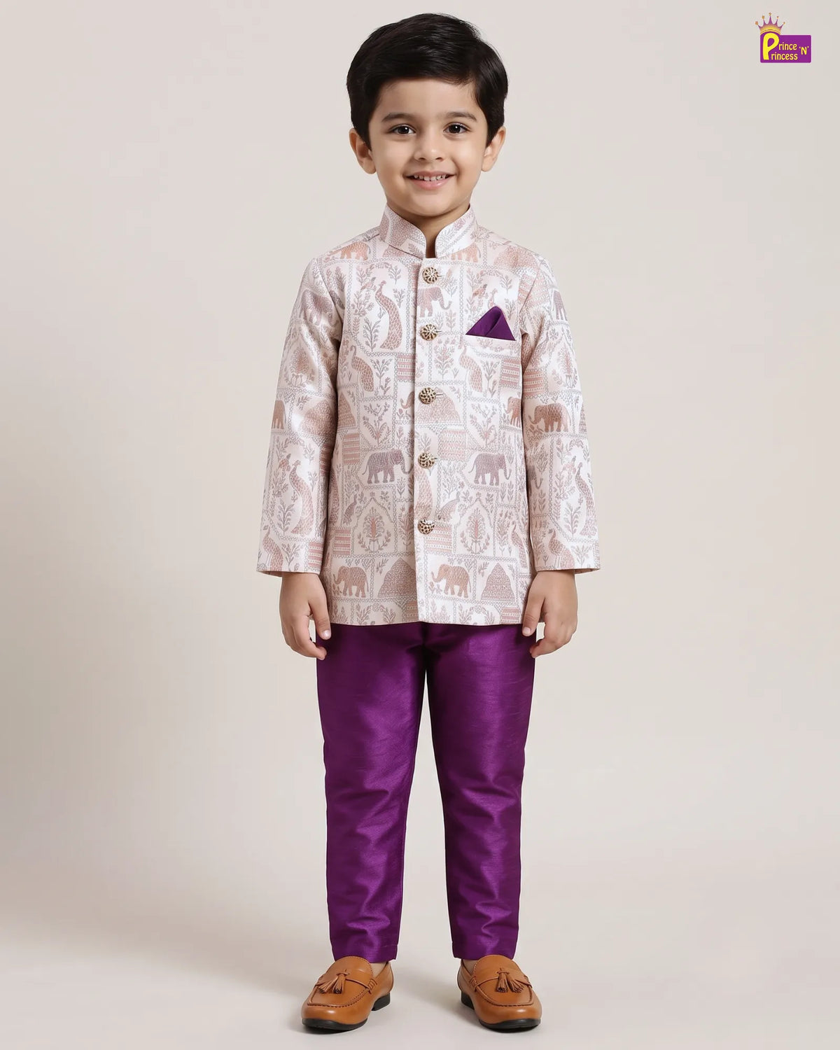 A young boy modeling a traditional Indian outfit consisting of a light beige and white patterned sherwani jacket with a purple pocket square, paired with solid purple trousers and brown tassel shoes, against a plain beige studio background.