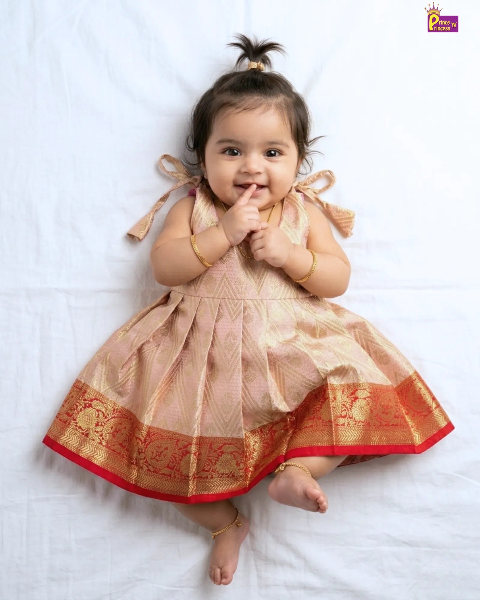 Baby wearing a traditional dress with gold and red patterns on a white background