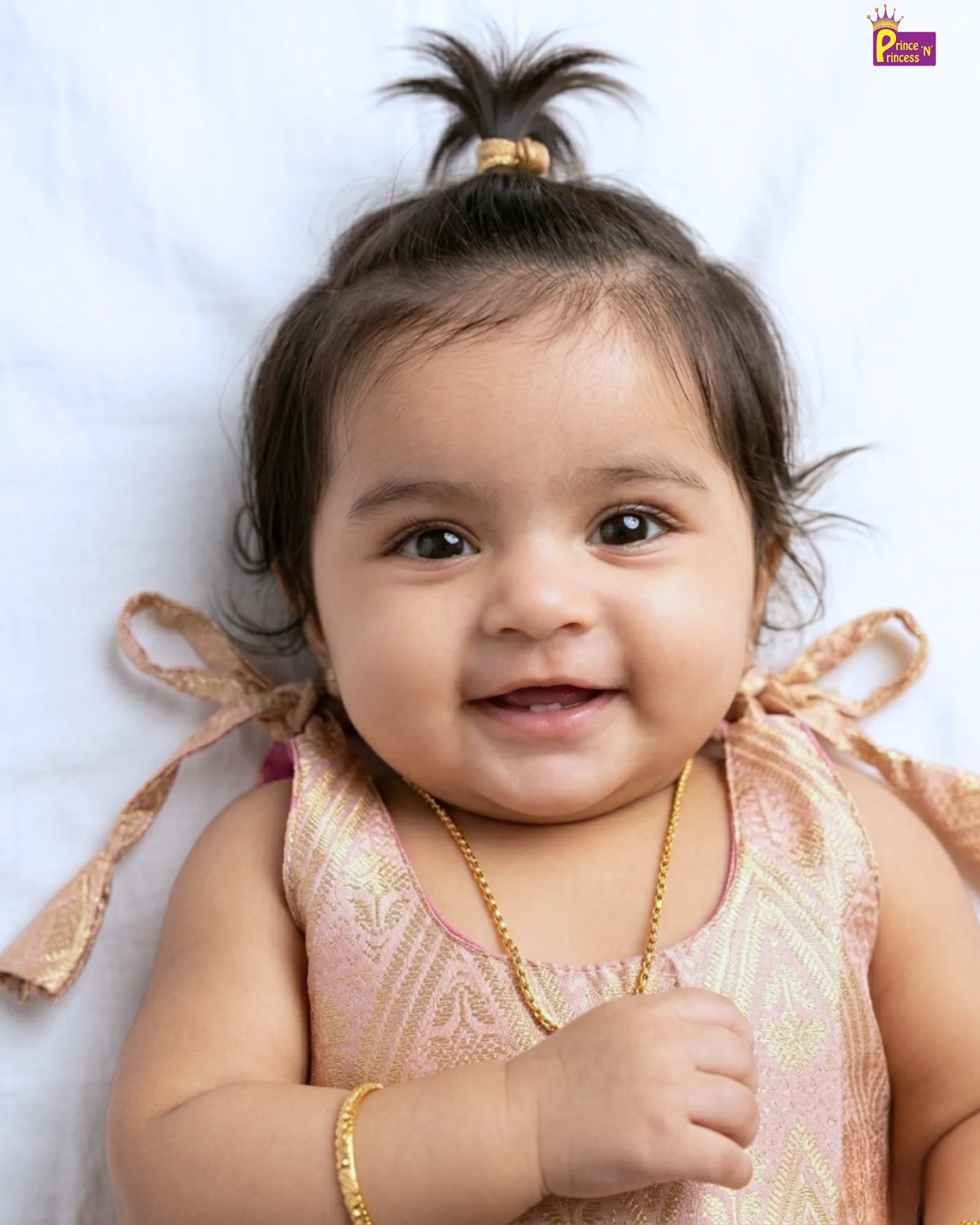 Baby wearing a pink outfit with gold accents on a white background