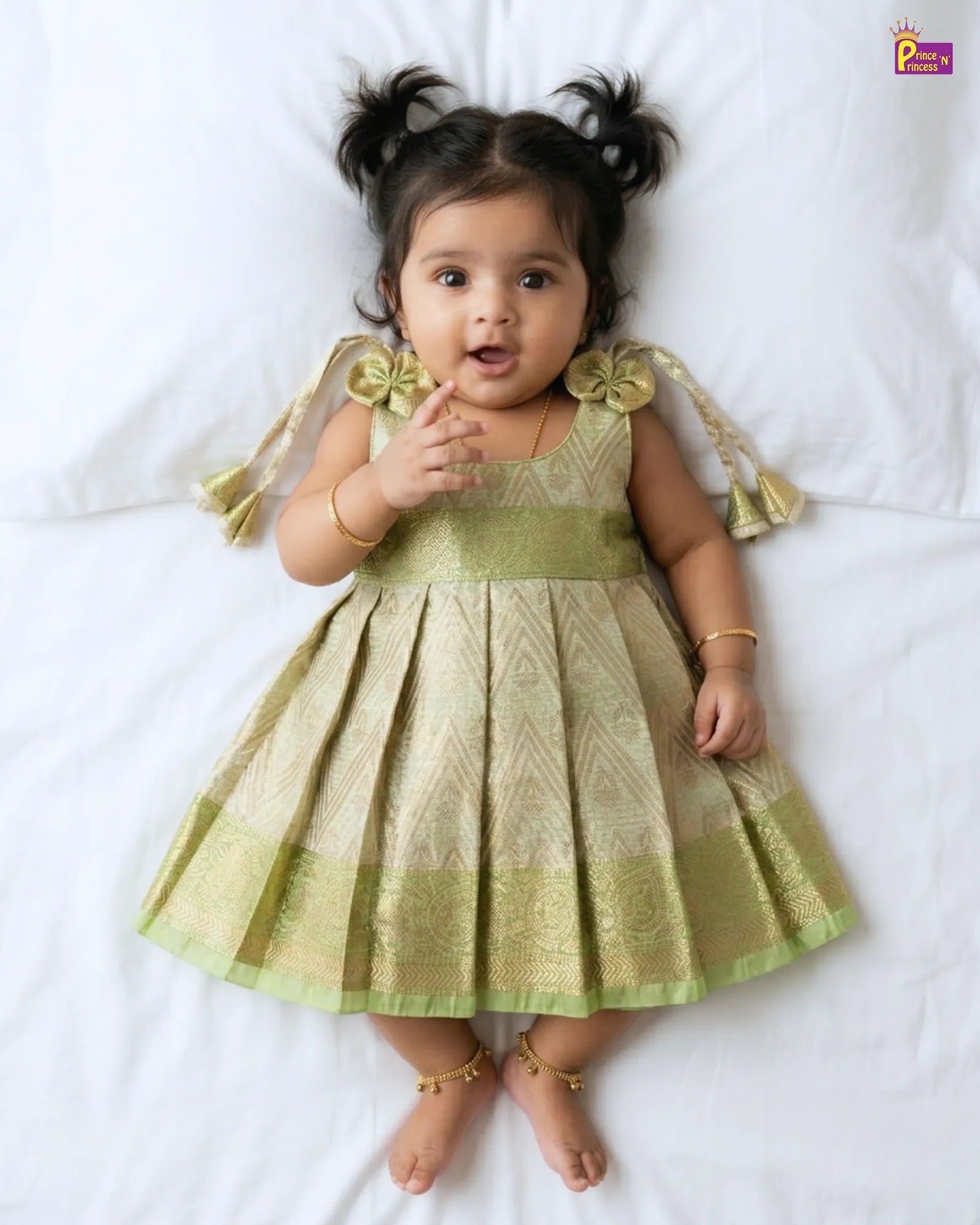 Baby wearing a green dress with decorative elements on a white background
