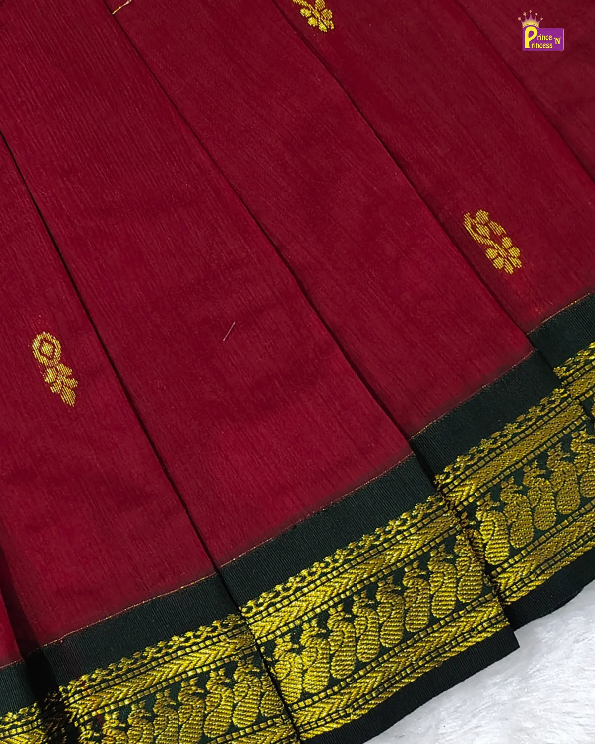 A close-up of a deep red or maroon fabric with a wide black border featuring intricate gold zari embroidery and motifs.
