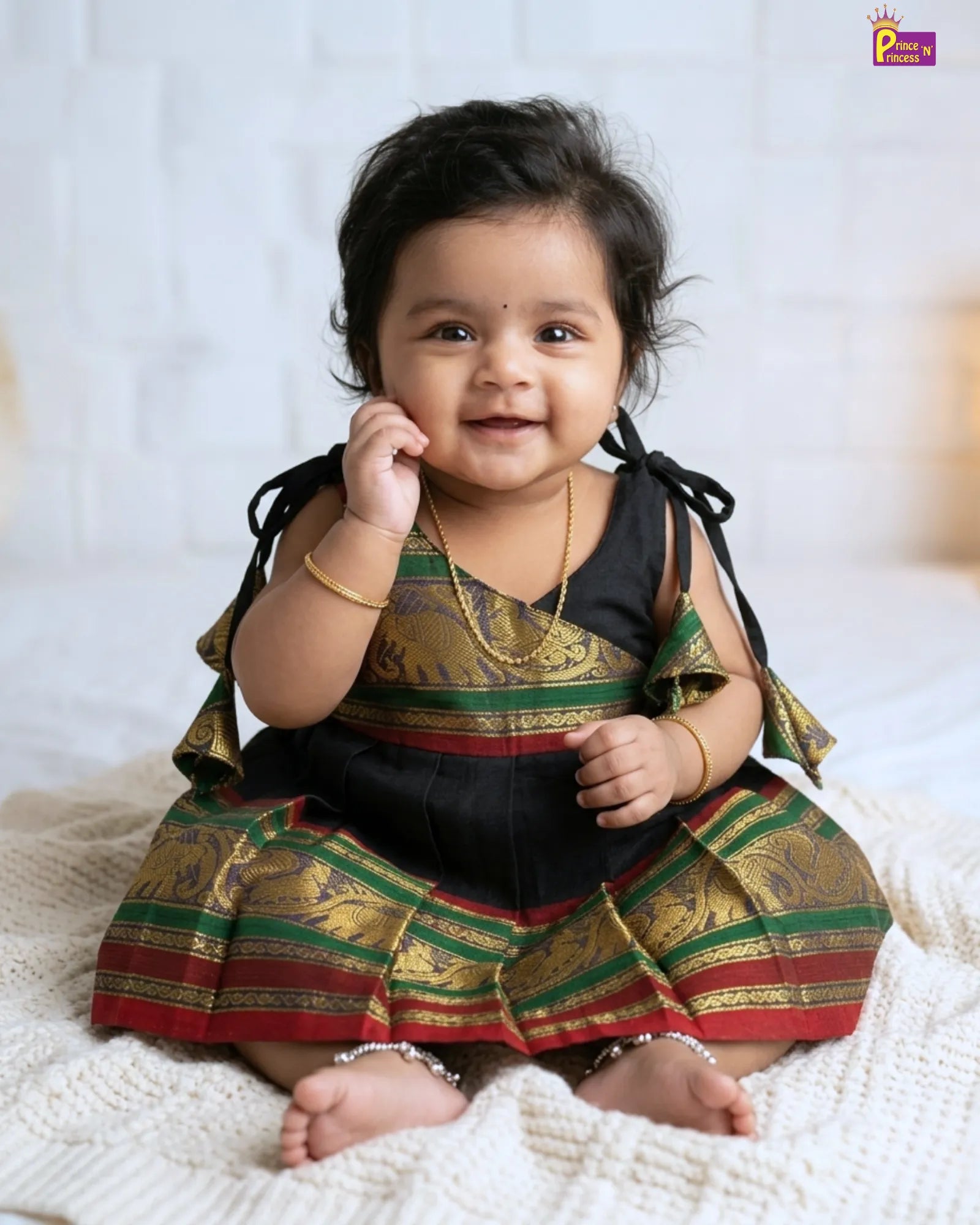 Baby wearing a traditional outfit with green and gold patterns on a white background