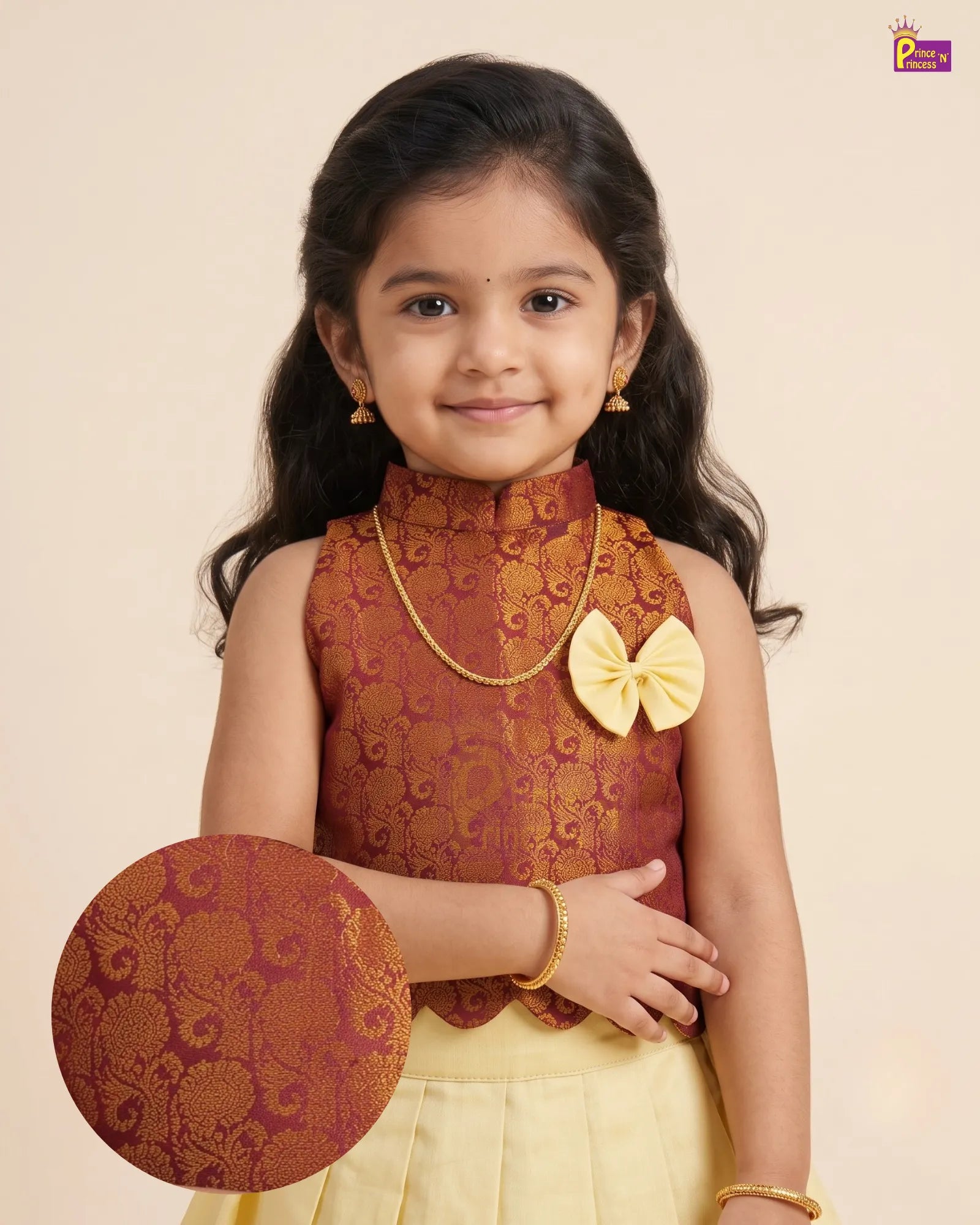 A young girl modeling a traditional Indian outfit consisting of a sleeveless rust-red and gold brocade top with a yellow bow accent, paired with a light yellow skirt. She is holding a round matching brocade plate.