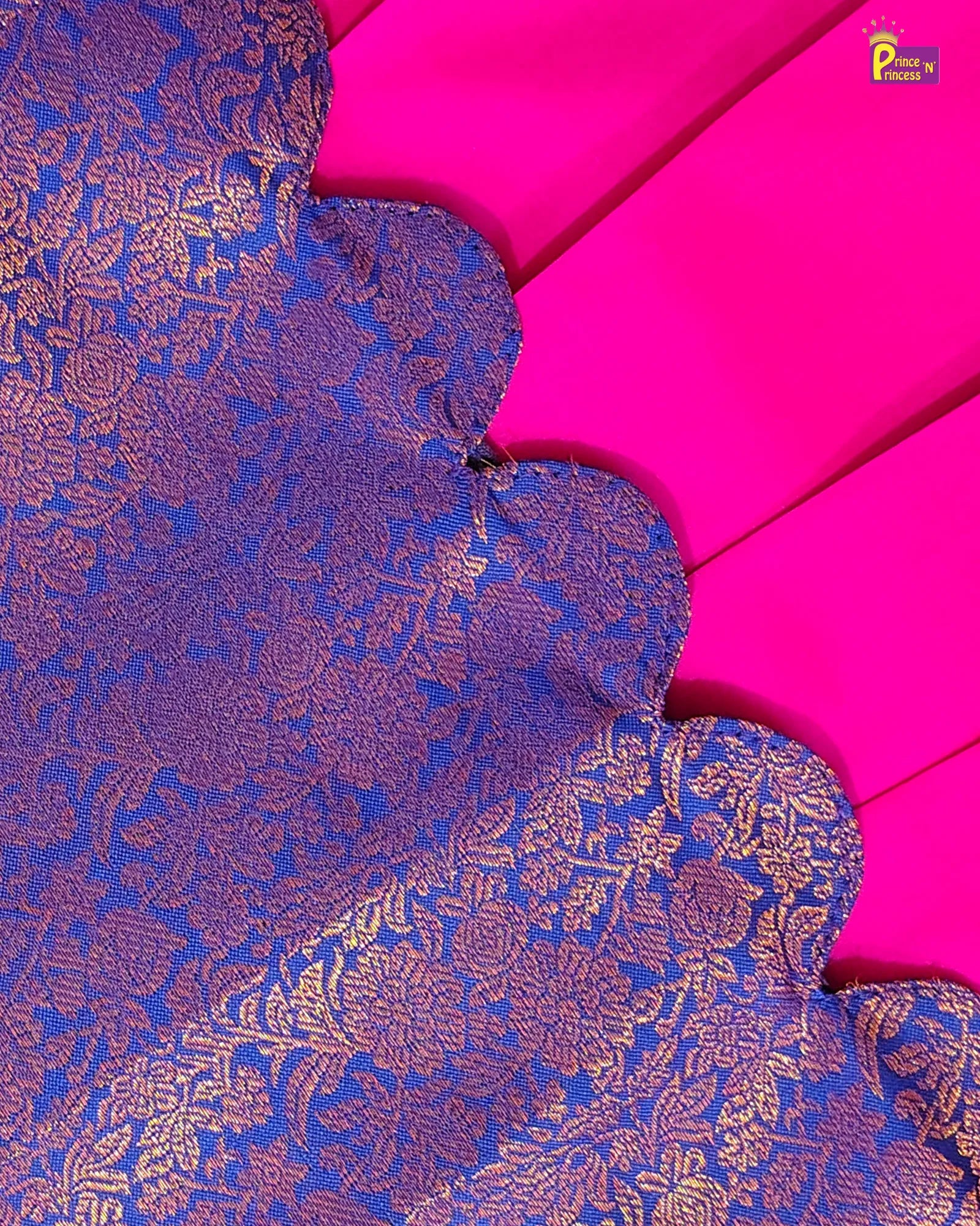 A close-up of a richly textured royal blue and gold brocade fabric with a scalloped edge, laid over a vibrant hot pink fabric background. A small 'Pune by Prashant' brand watermark is visible in the top right corner.
