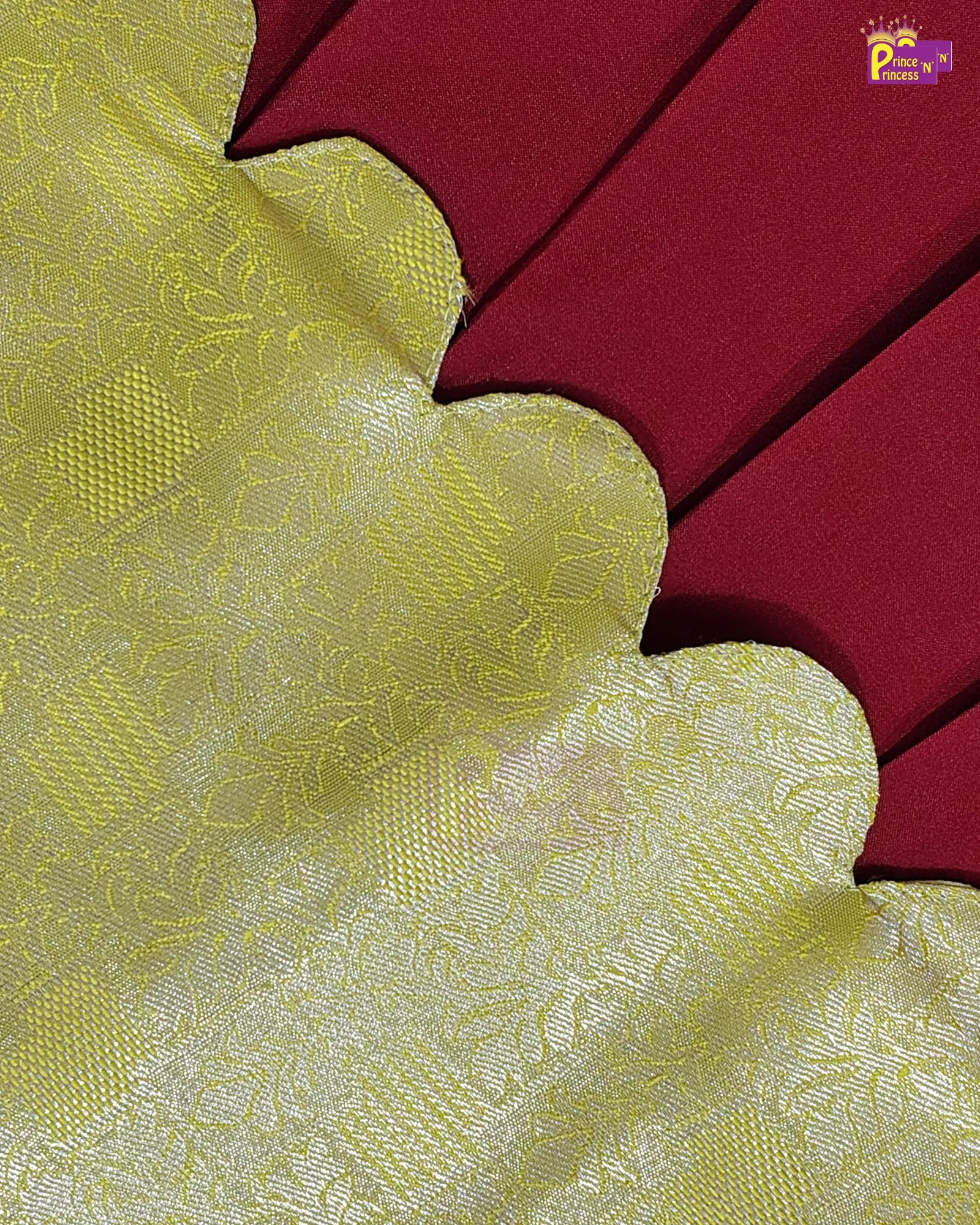 A close-up of a fabric product showing a yellow-gold scalloped border with a subtle woven floral pattern, layered over a deep red background.