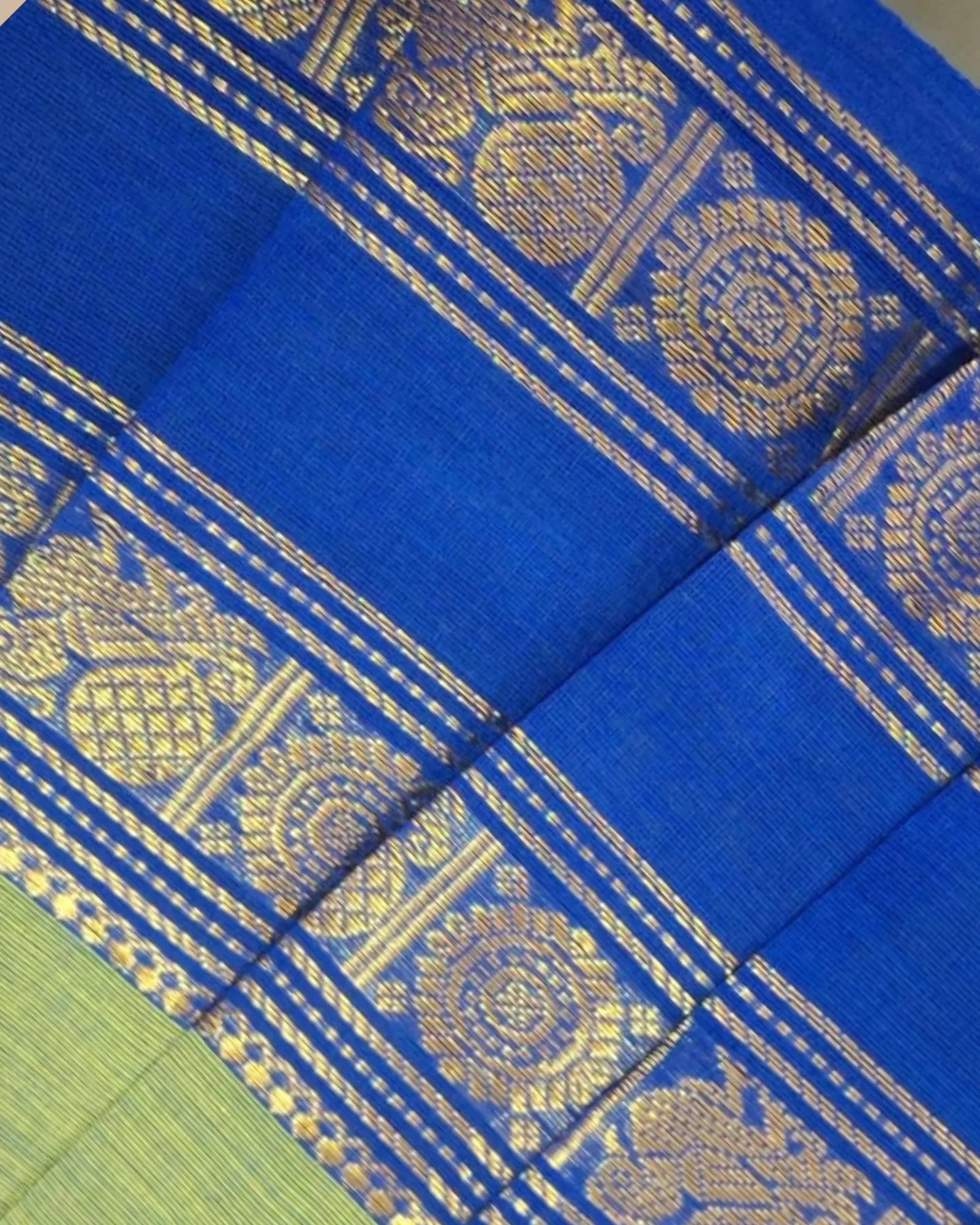 A close-up of a royal blue fabric with intricate gold zari woven patterns and borders, showing the texture and detail of the textile.