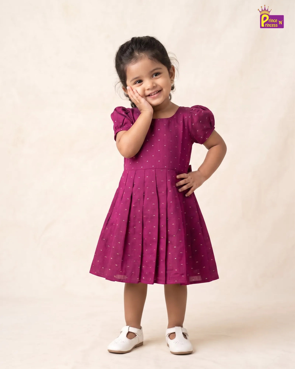 A young girl modeling a magenta pink short-sleeve dress with small white polka dots, standing against a warm beige textured backdrop. She is wearing white Mary Jane shoes, and a 'Place de Paris' logo is visible in the top right corner.