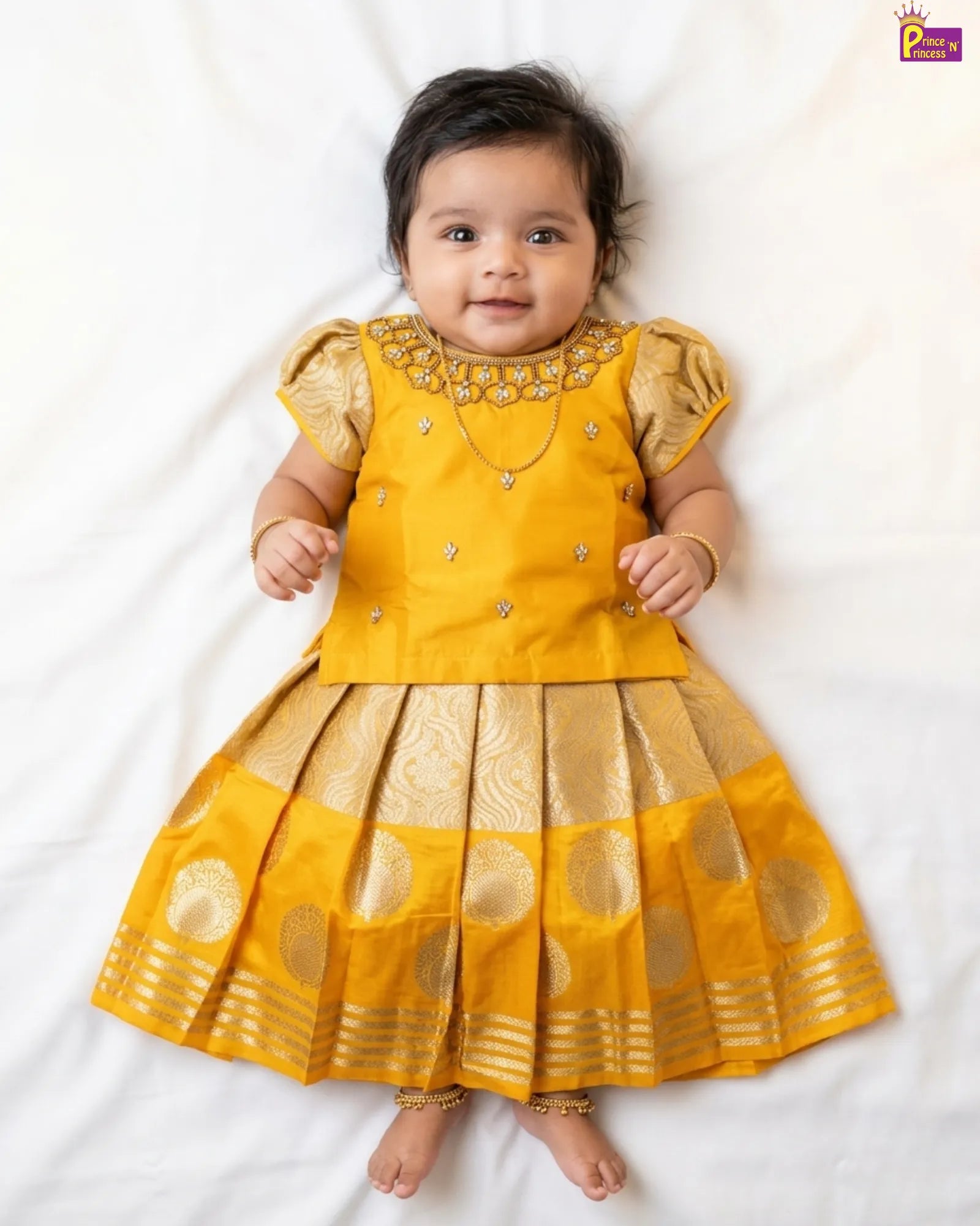Baby wearing a yellow traditional outfit with intricate designs on a white background