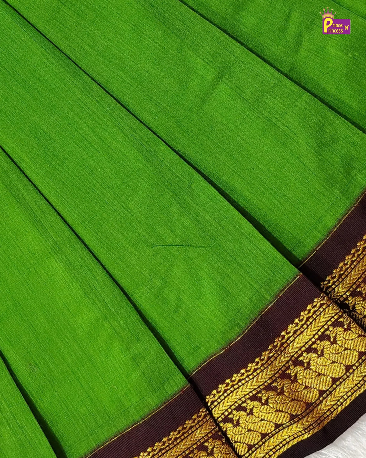 A close-up of a bright green silk saree with a dark brown border featuring intricate gold zari embroidery.