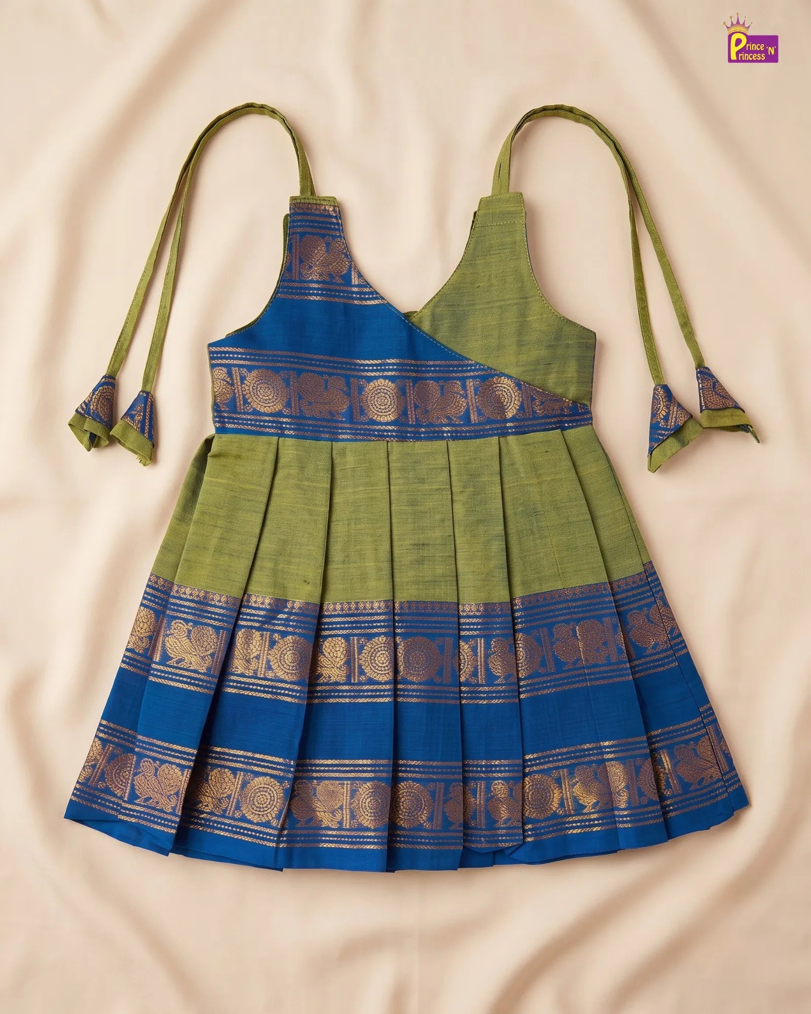 A sleeveless pleated dress with olive green and royal blue horizontal bands, decorated with gold zari patterns, laid flat on a beige fabric background.
