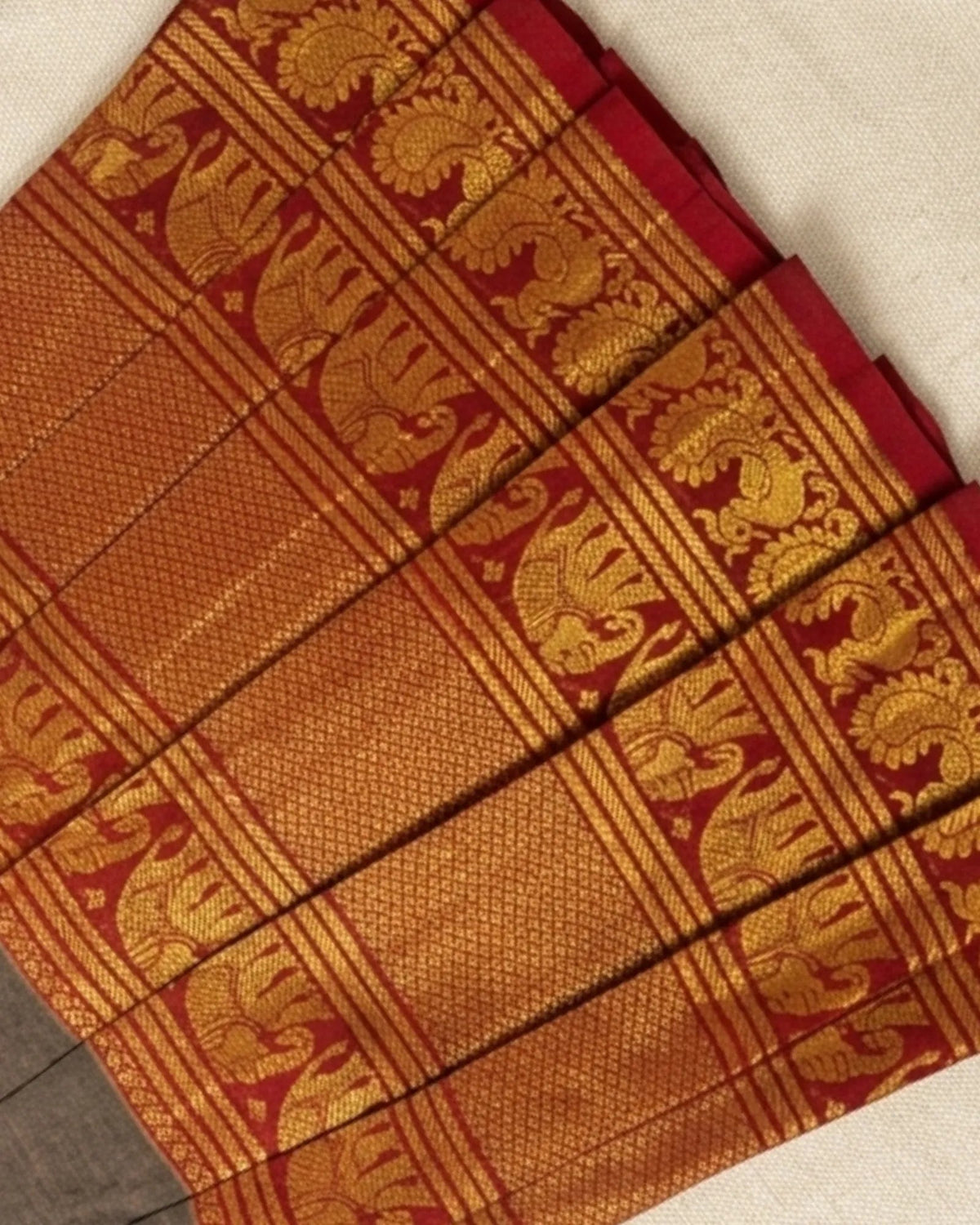 A close-up of a folded traditional Indian silk saree, showcasing its rich golden-yellow body with intricate red and gold woven floral patterns.