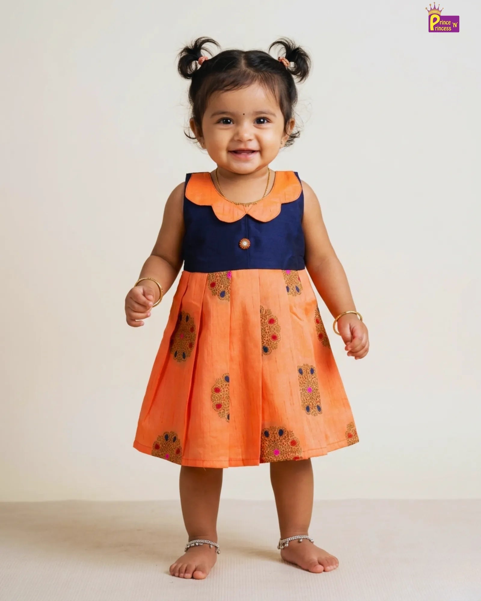 Child wearing an orange and navy dress with floral patterns on a white background