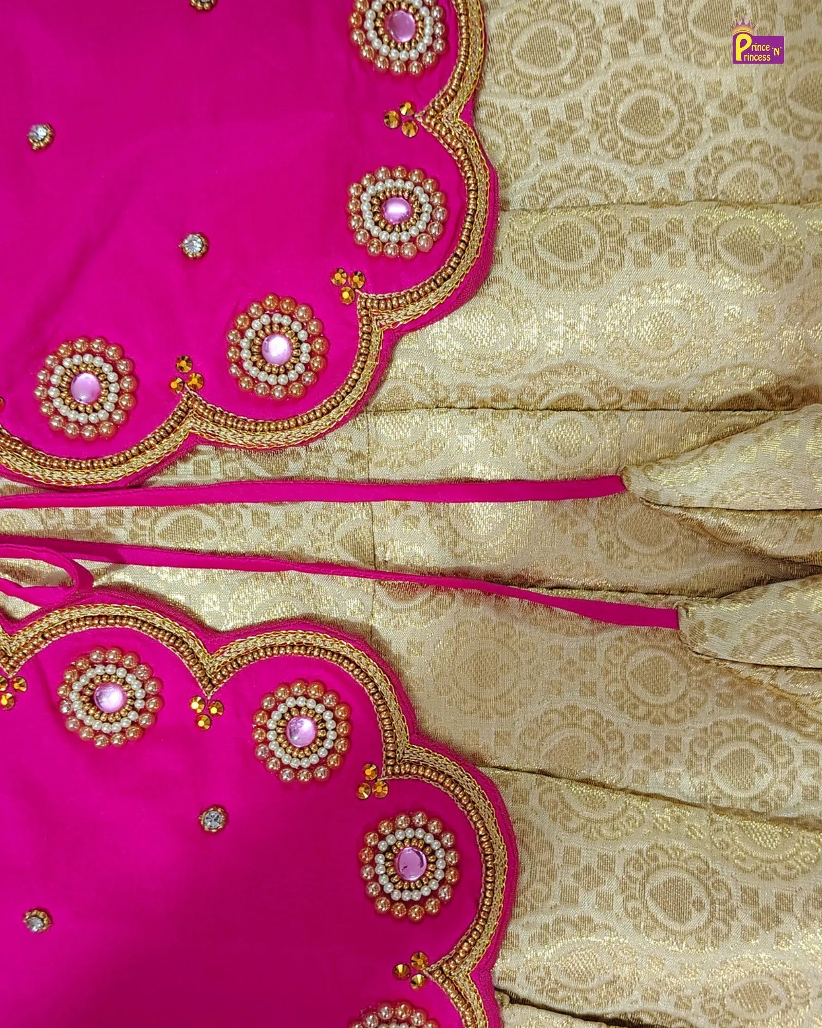 A close-up of a traditional Indian outfit fabric, featuring a bright pink dupatta with gold zari embroidery and mirror work, paired with a beige and gold brocade saree body.