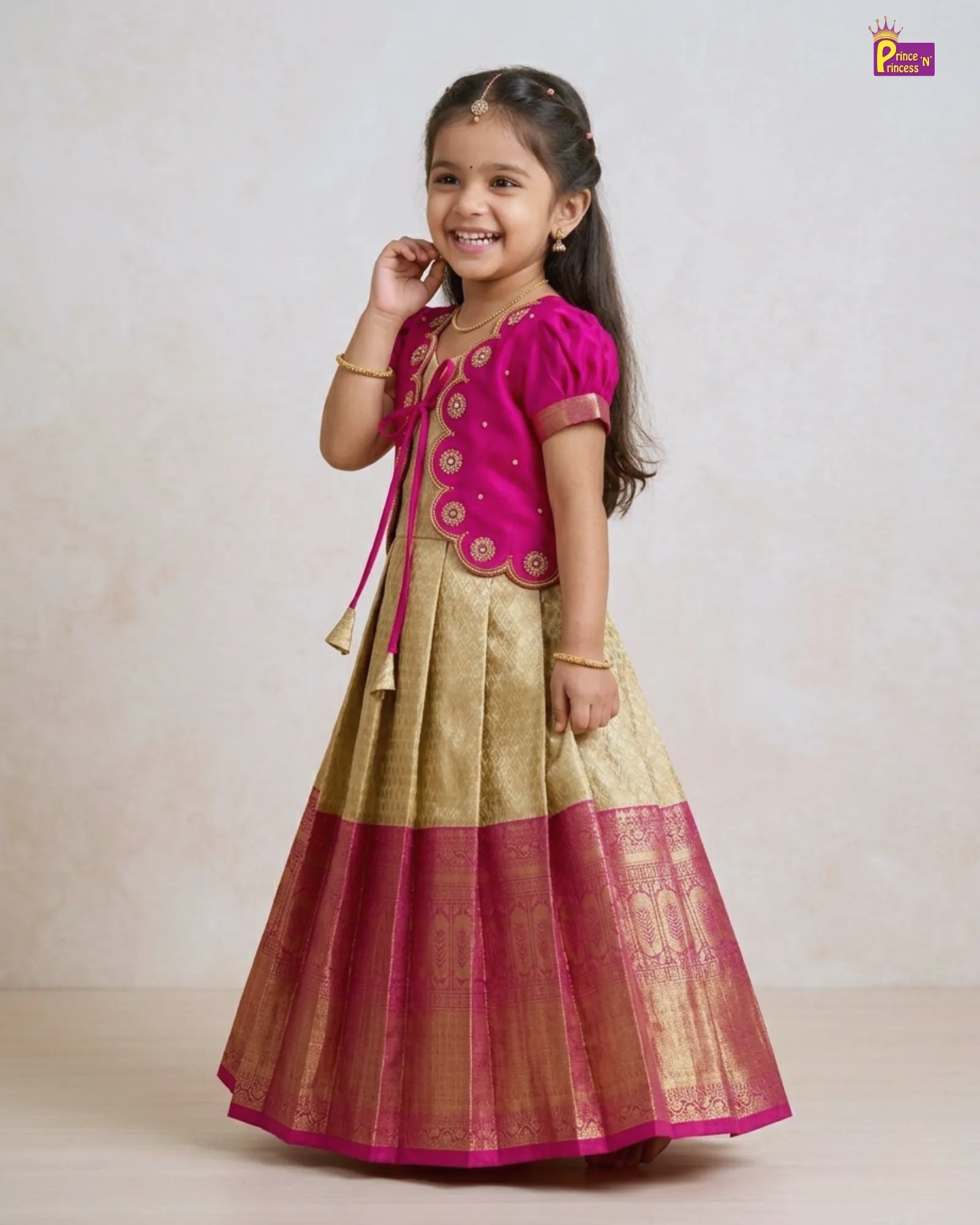 Young girl wearing a traditional outfit with a pink top and gold skirt on a plain background