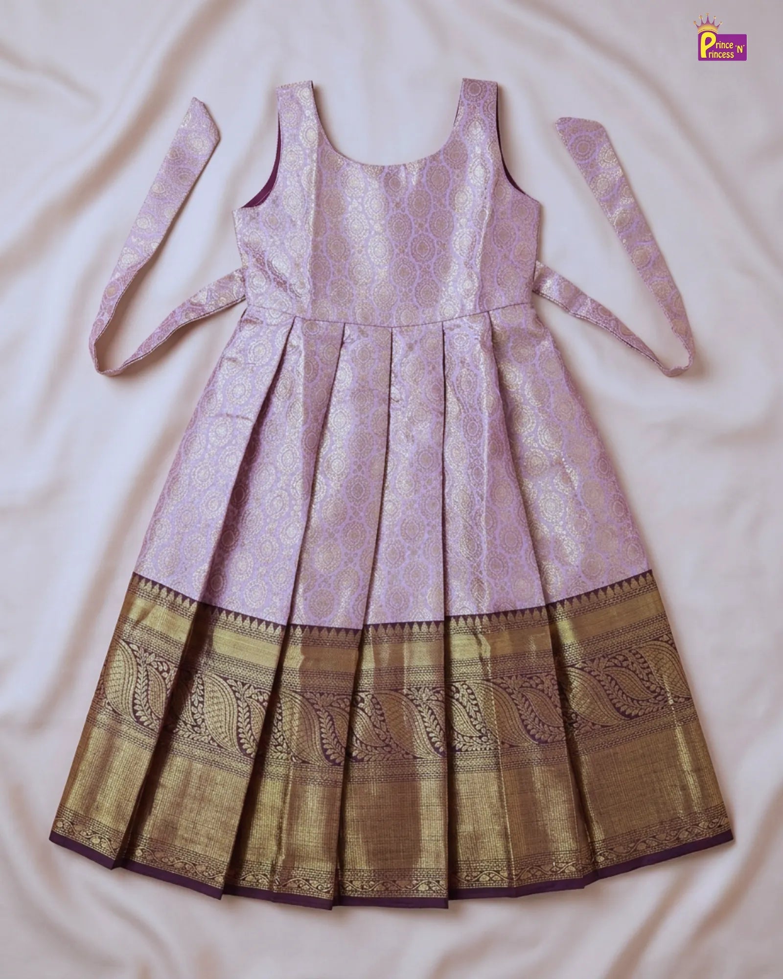 A sleeveless traditional Indian dress with a light purple/lavender body and a wide gold zari border, laid flat on a white fabric background.