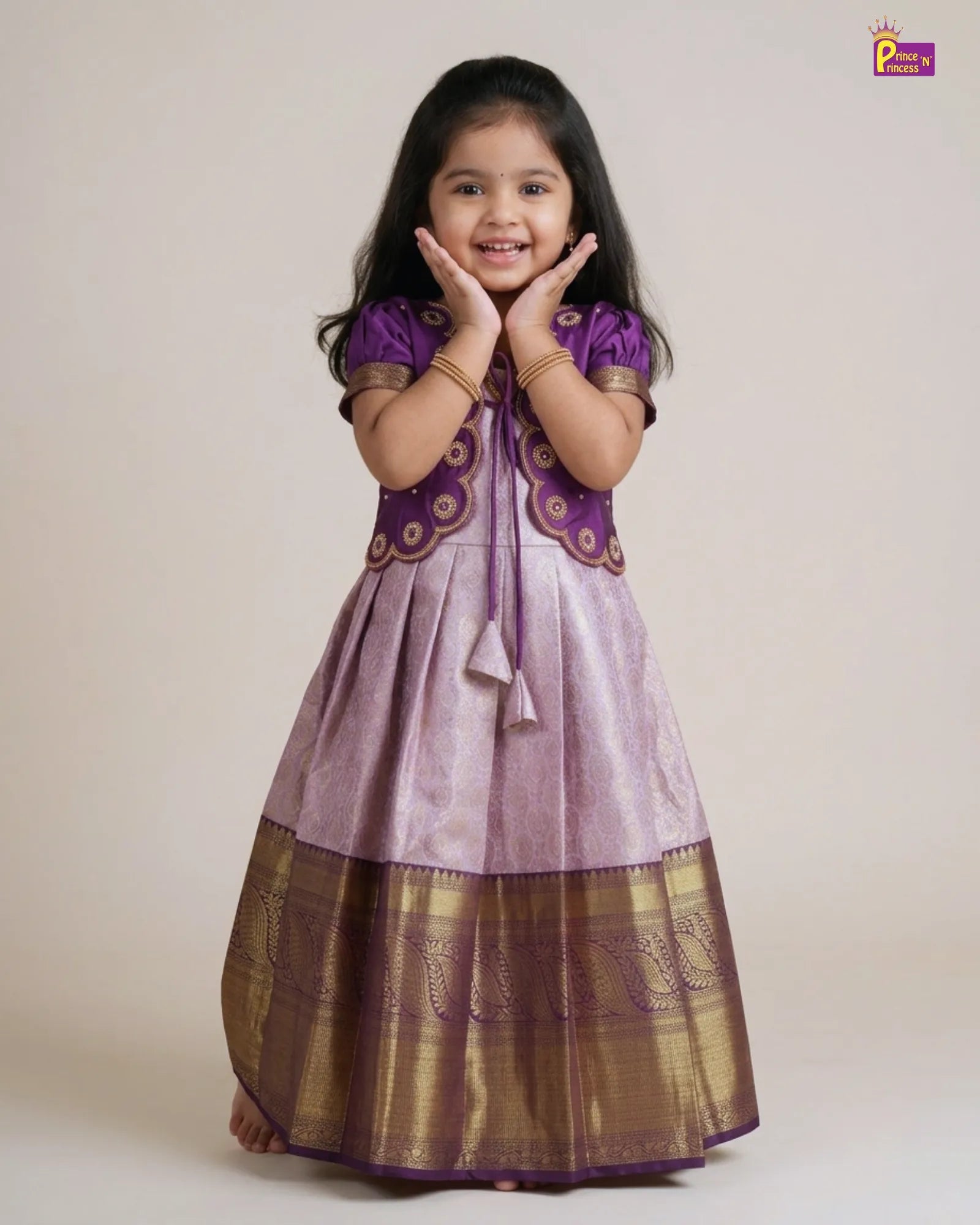 A young girl modeling a traditional Indian salwar kameez dress. The dress features a lavender-purple body with a wide metallic gold border at the hem, a matching purple embroidered yoke, and purple sleeves.