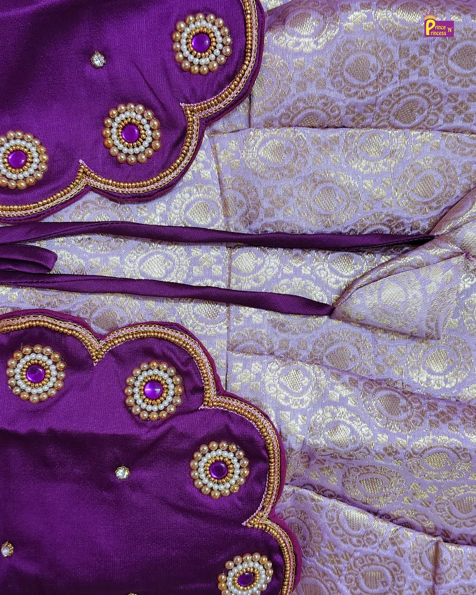 Close-up of a purple and lavender brocade fabric with gold zari patterns, scalloped edges, and embroidered circular motifs with purple centers and gold beadwork.