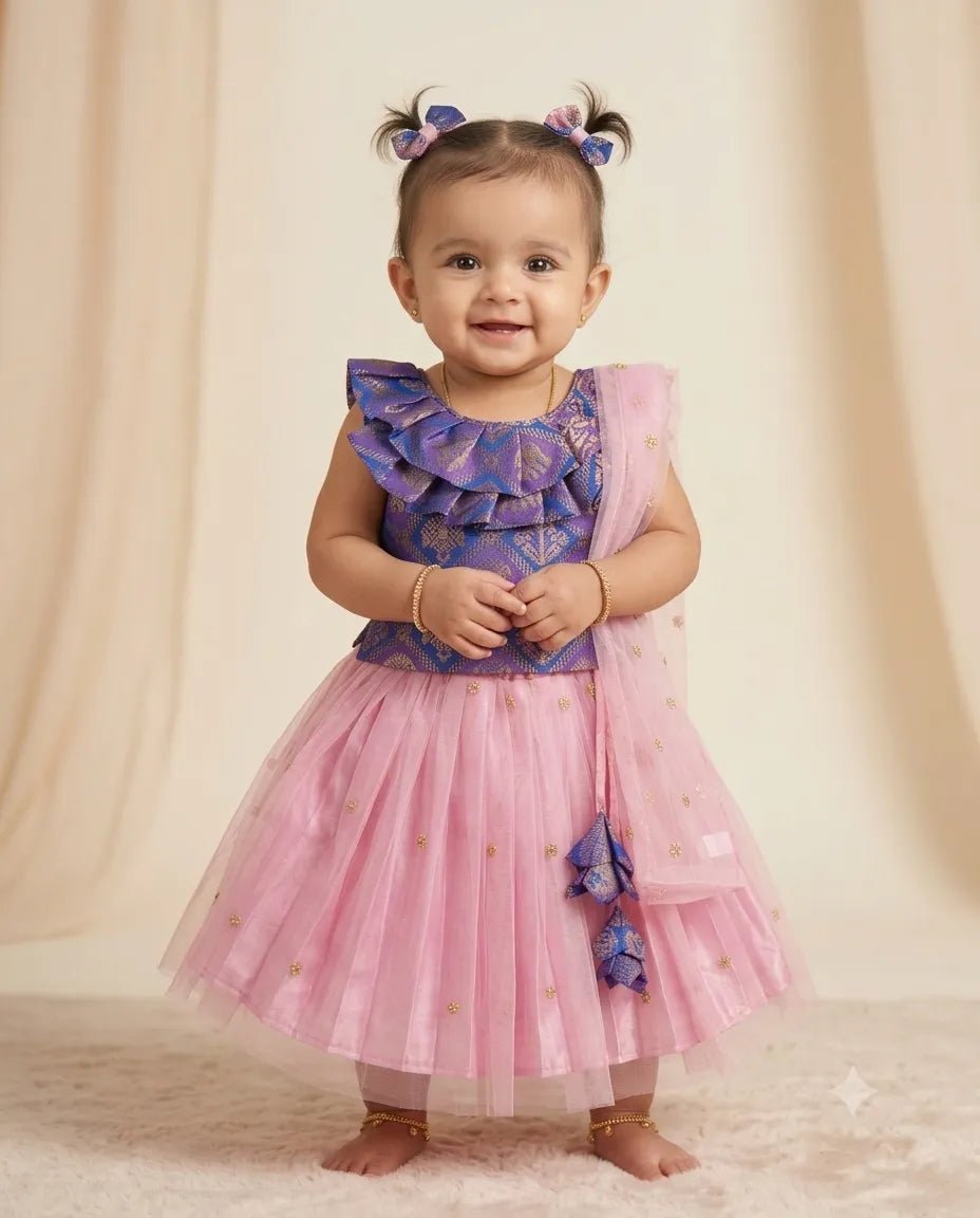 A toddler girl wearing a two-piece dress with a purple patterned ruffled top and a pink tulle skirt with gold star details, standing against a beige draped backdrop.