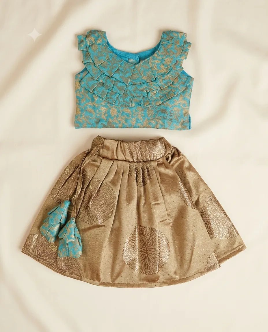 A two-piece toddler girl's ethnic outfit set featuring a turquoise blue ruffled blouse with gold foil patterns and a matching pleated gold skirt with a small turquoise bow, laid flat on a cream fabric background.