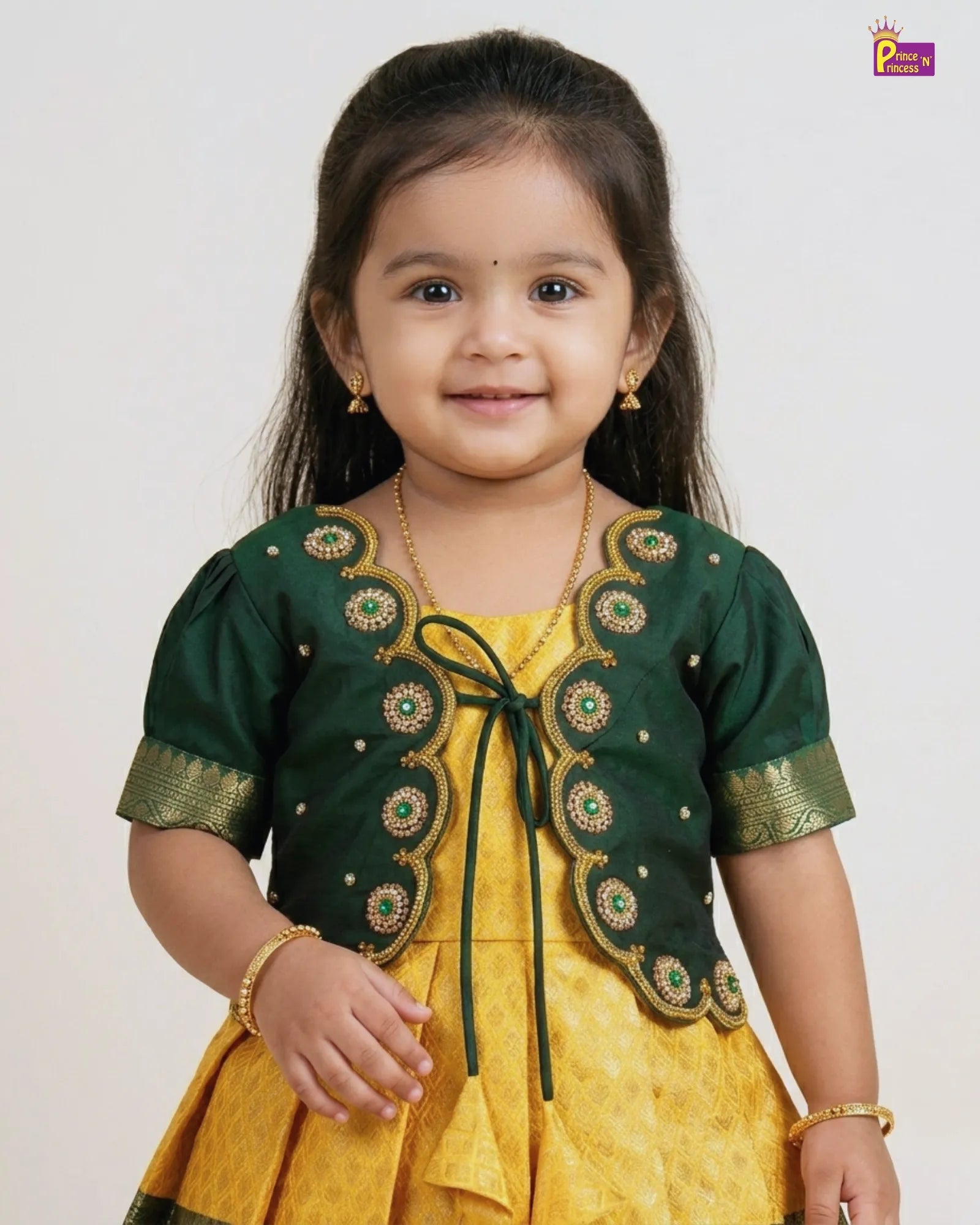 Child wearing a green embroidered shrug over a yellow dress on a white background