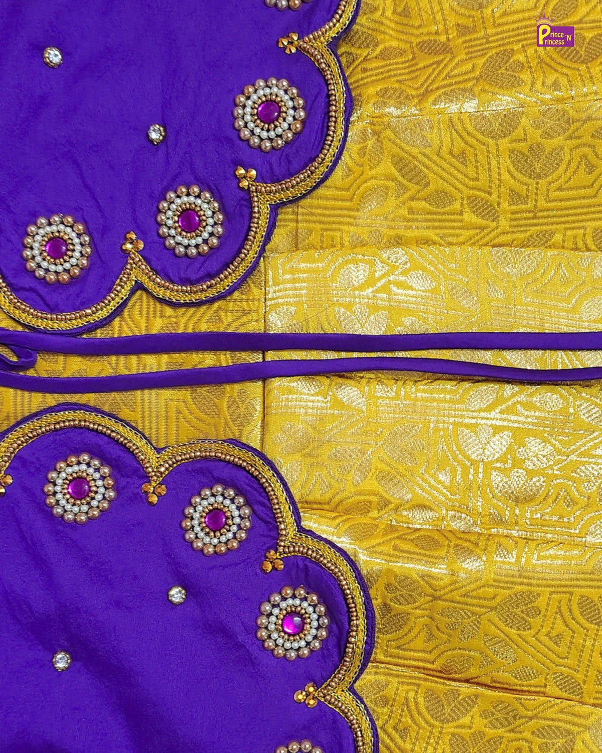 A close-up of a purple and yellow fabric textile, likely a saree or scarf, featuring a richly patterned yellow body with silver zari motifs and matching purple borders decorated with scalloped edges, gold embroidery, and pink gemstone accents.