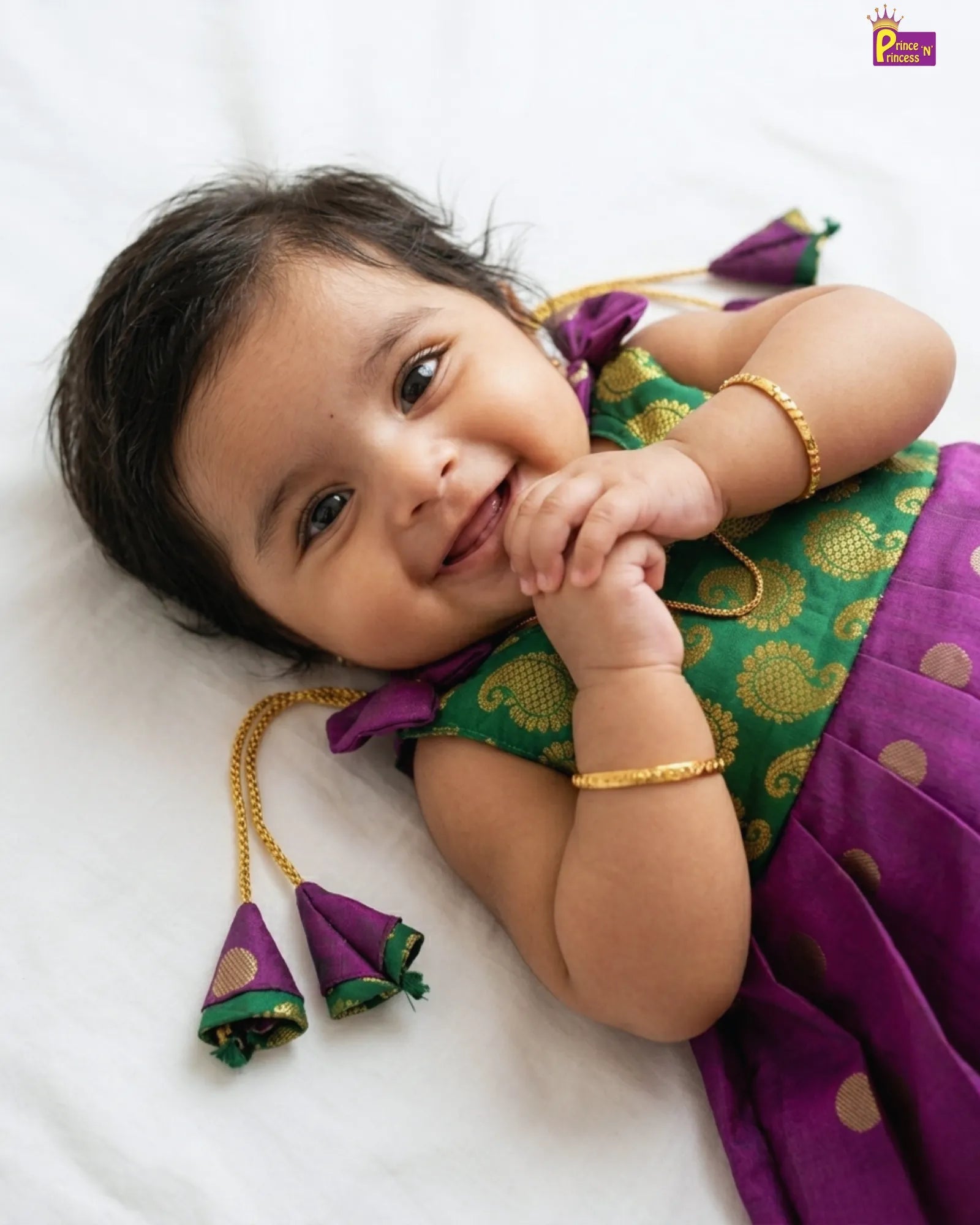 Baby in a green and purple traditional outfit with gold jewelry on a white background