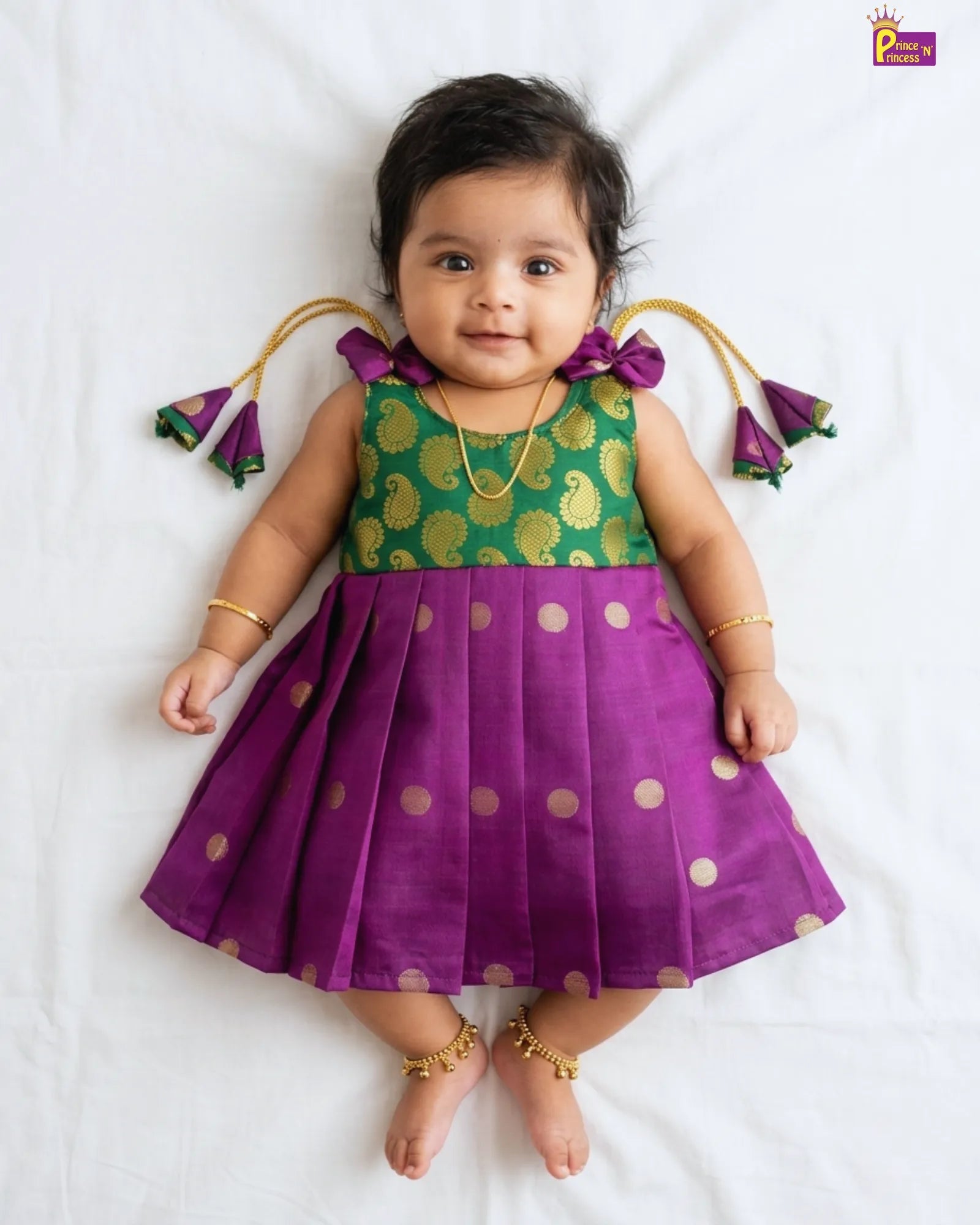Baby wearing a green and purple traditional outfit with gold polka dots on a white background