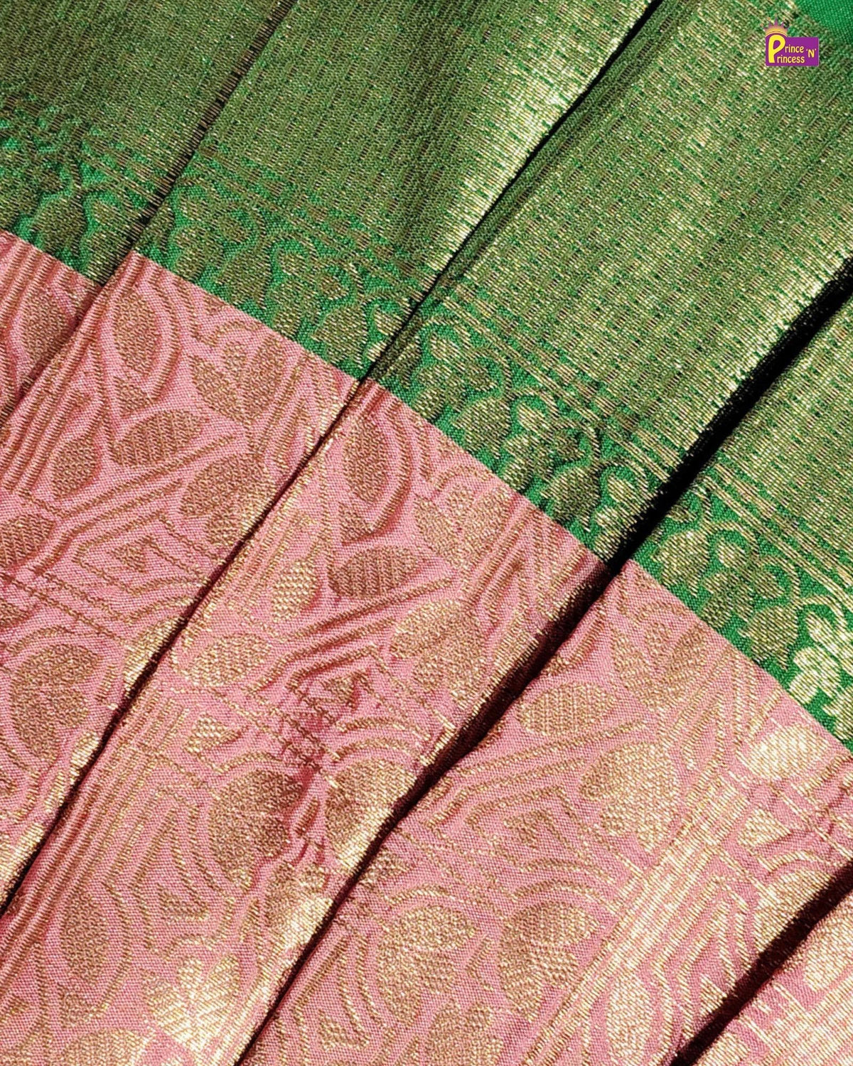 Close-up of a woven textile with a green upper section and a pink lower section, both featuring metallic gold zari floral and geometric patterns.