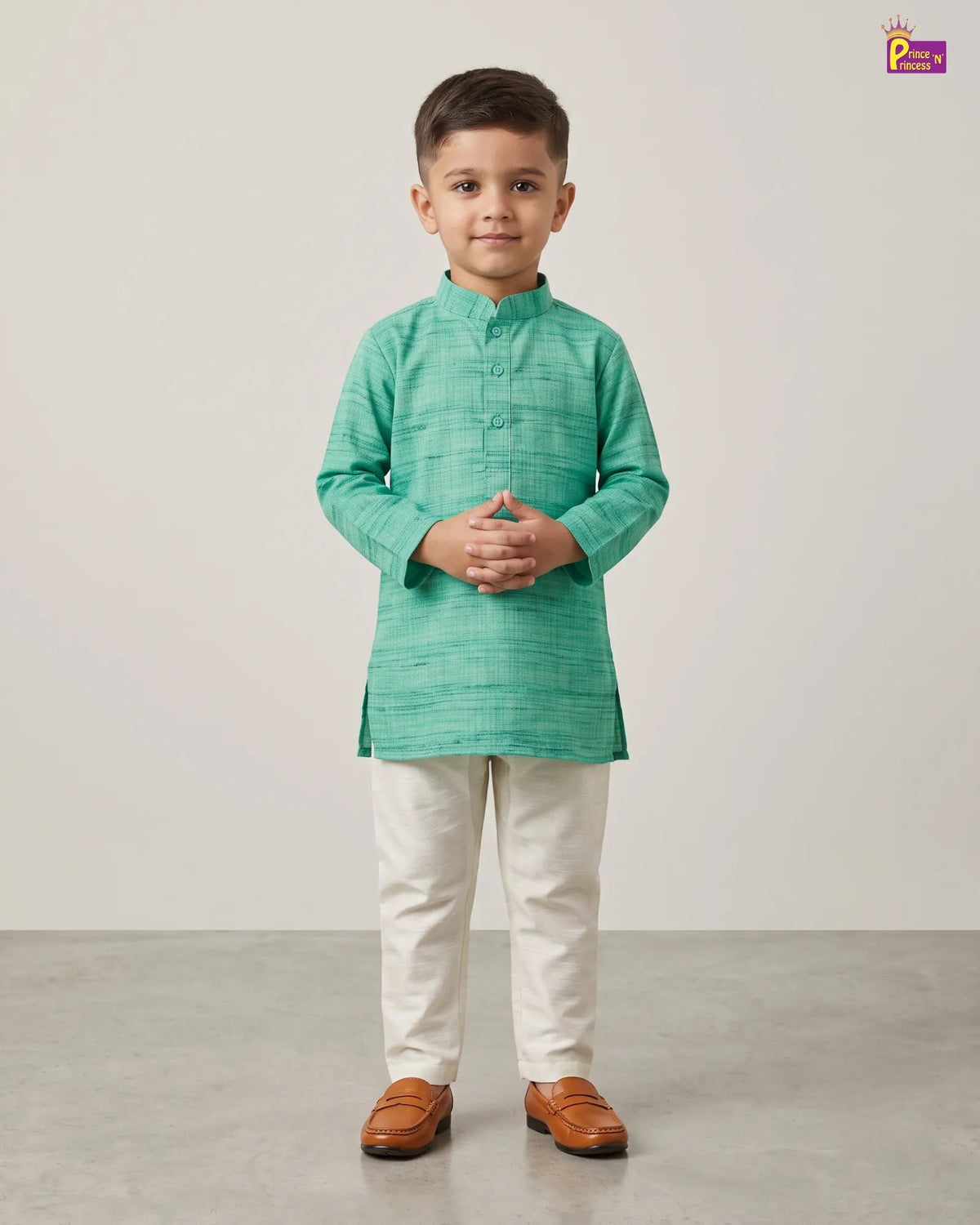 A young boy modeling a mint green textured kurta with cream trousers and brown leather loafers, standing against a neutral studio backdrop.