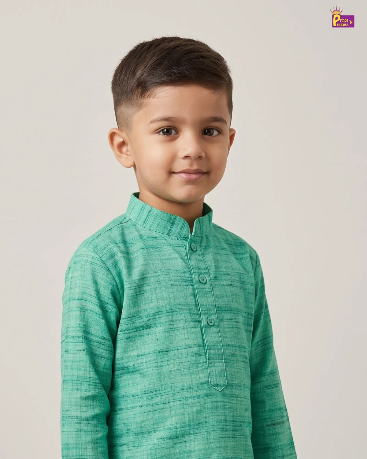 A young boy wearing a green textured long-sleeve kurta with a mandarin collar, standing against a plain light beige background.